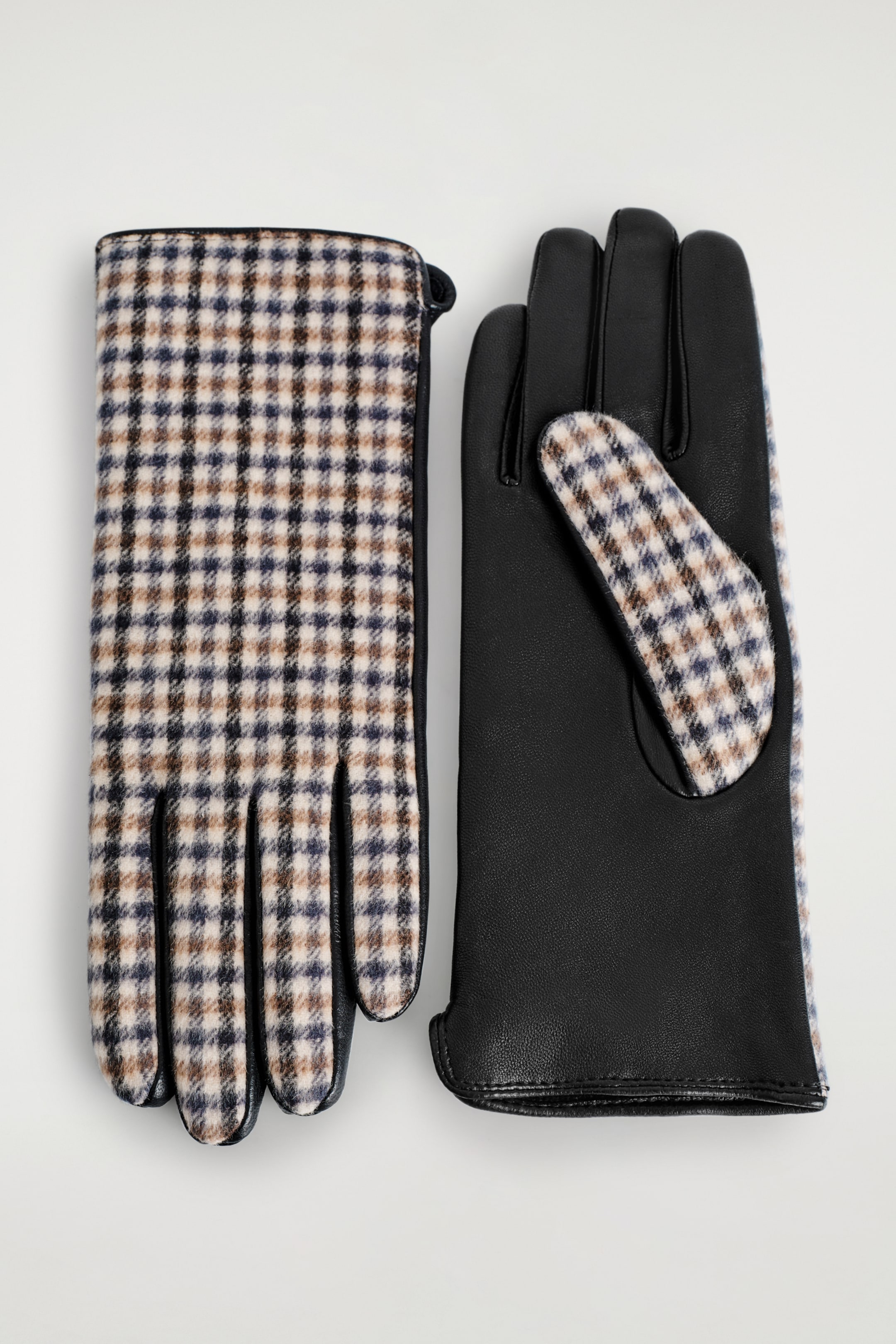 View larger image: A pair of gloves is lying flat, displaying a contrasting design of black leather and a beige, brown, and dark blue small-check pattern. The glove on the left is showing its top side with the checkered pattern on the back and black leather fingers, while the glove on the right is revealing its black leather palm with a matching checkered panel near the thumb.