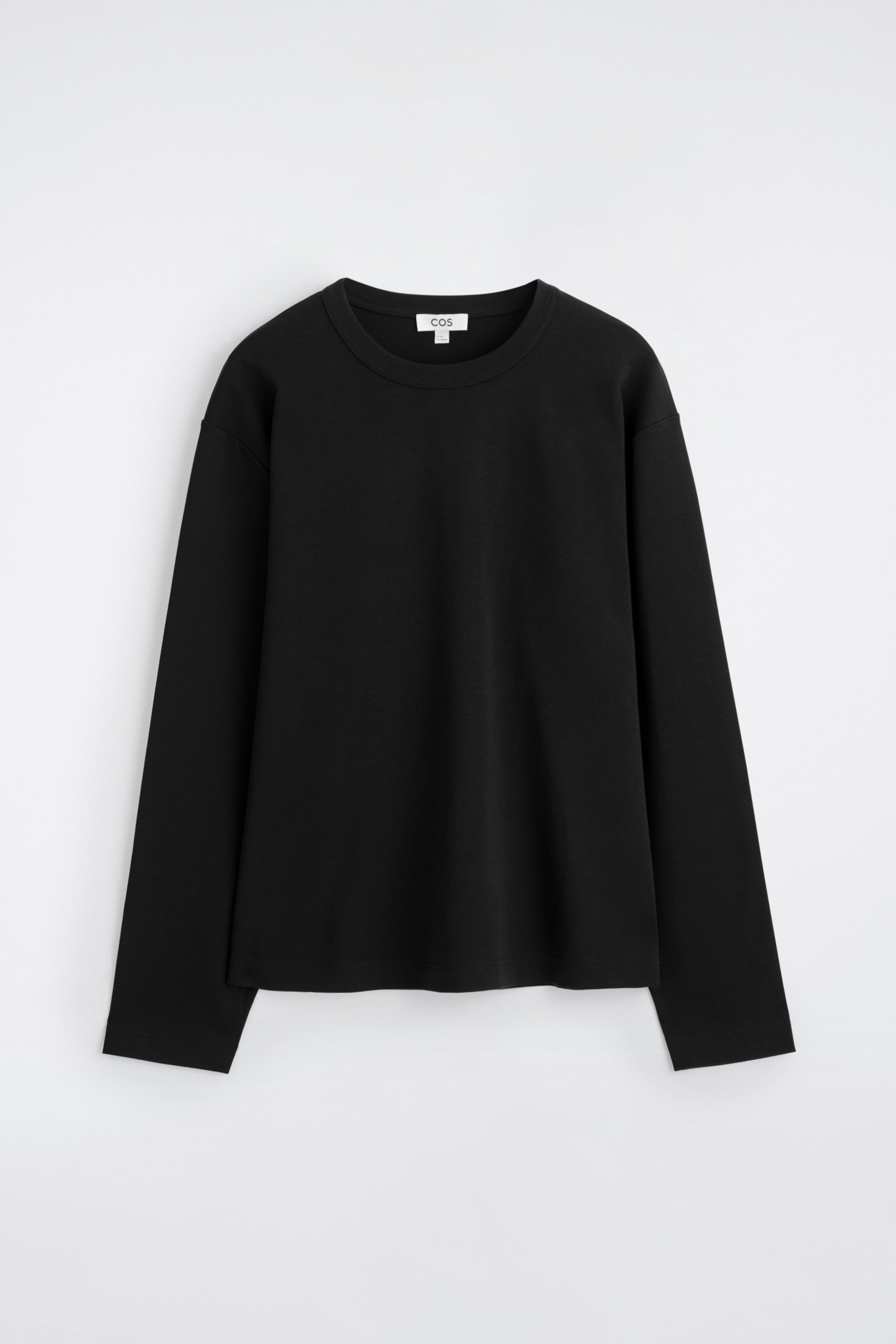 Größeres Bild ansehen: Ein schwarzes Langarm-T-Shirt ist von vorne zu sehen und zeigt eine entspannte Passform sowie einen klassischen Rundhalsausschnitt. Es besteht aus einem glatten, dunklen Stoff, hat einen geraden Saum und ein kleines weißes Markenschild, das am hinteren Halsausschnitt sichtbar ist.