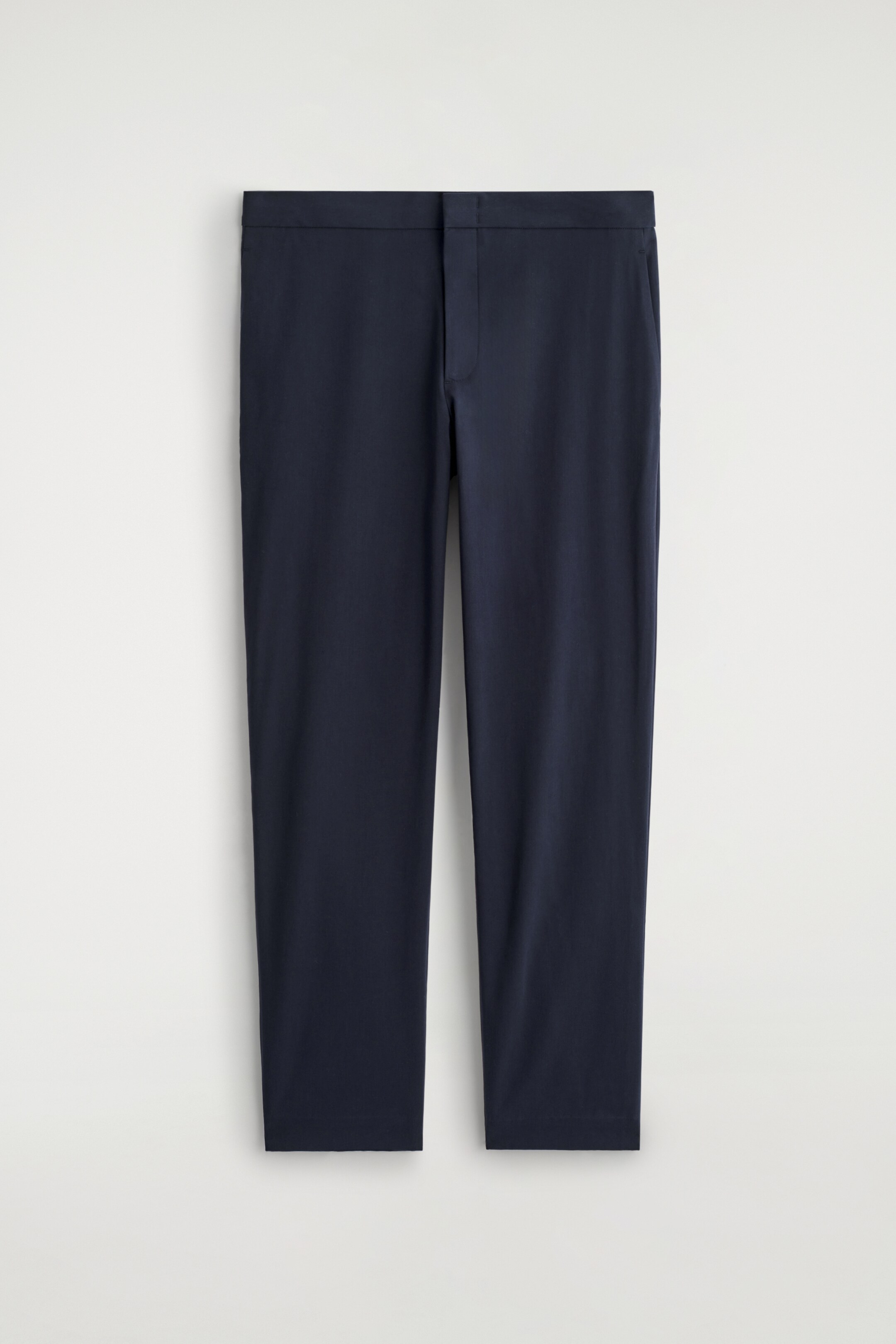 View larger image: A pair of dark blue slim-fit trousers is being displayed from the front. They are designed with a flat front, a smooth, unadorned waistband, and no visible pockets.