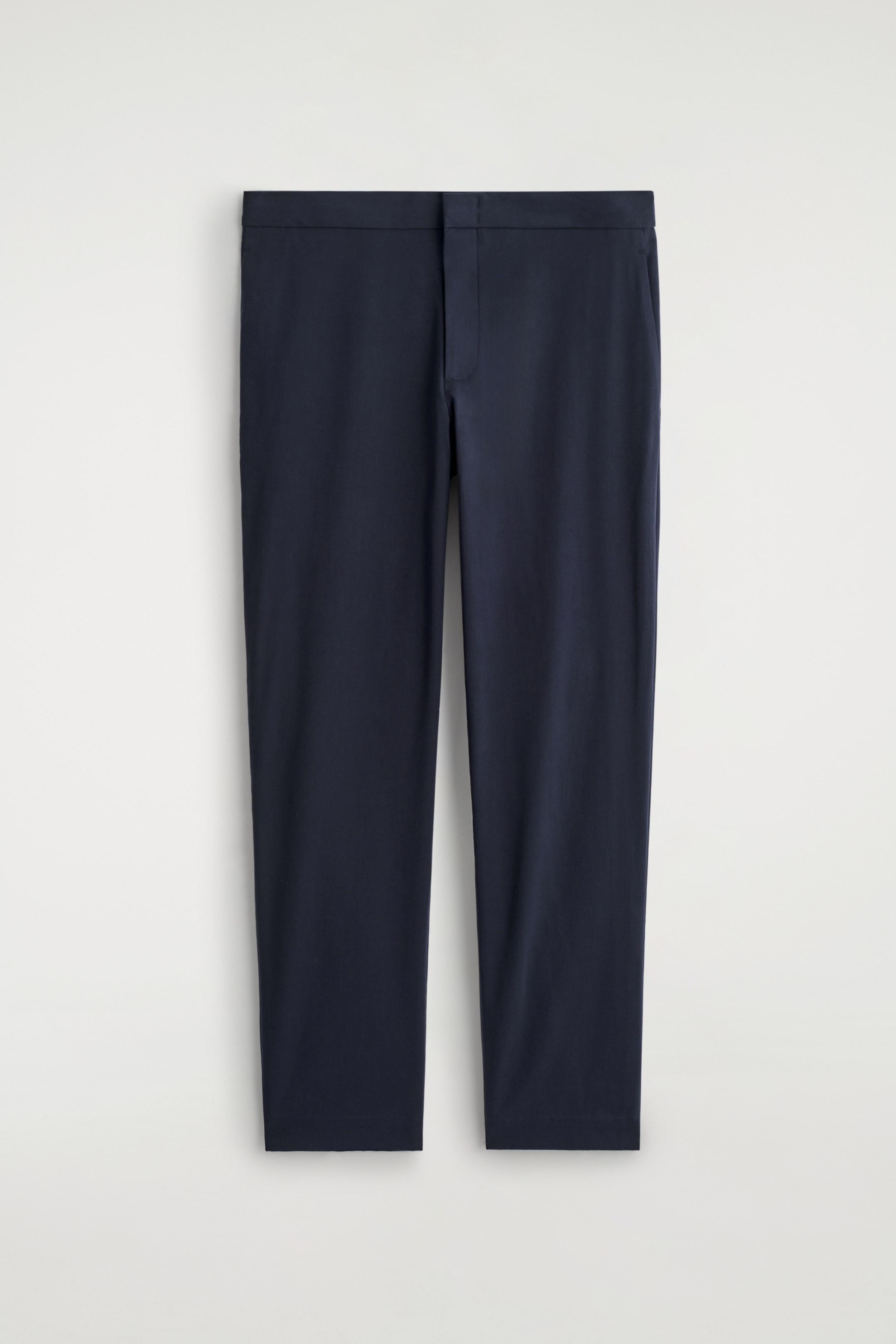 Vezi imaginea mai mare: O pereche de pantaloni slim-fit de culoare albastru închis este expusă din față. Sunt proiectați cu un front plat, o talie netedă, neornamentată și fără buzunare vizibile.
