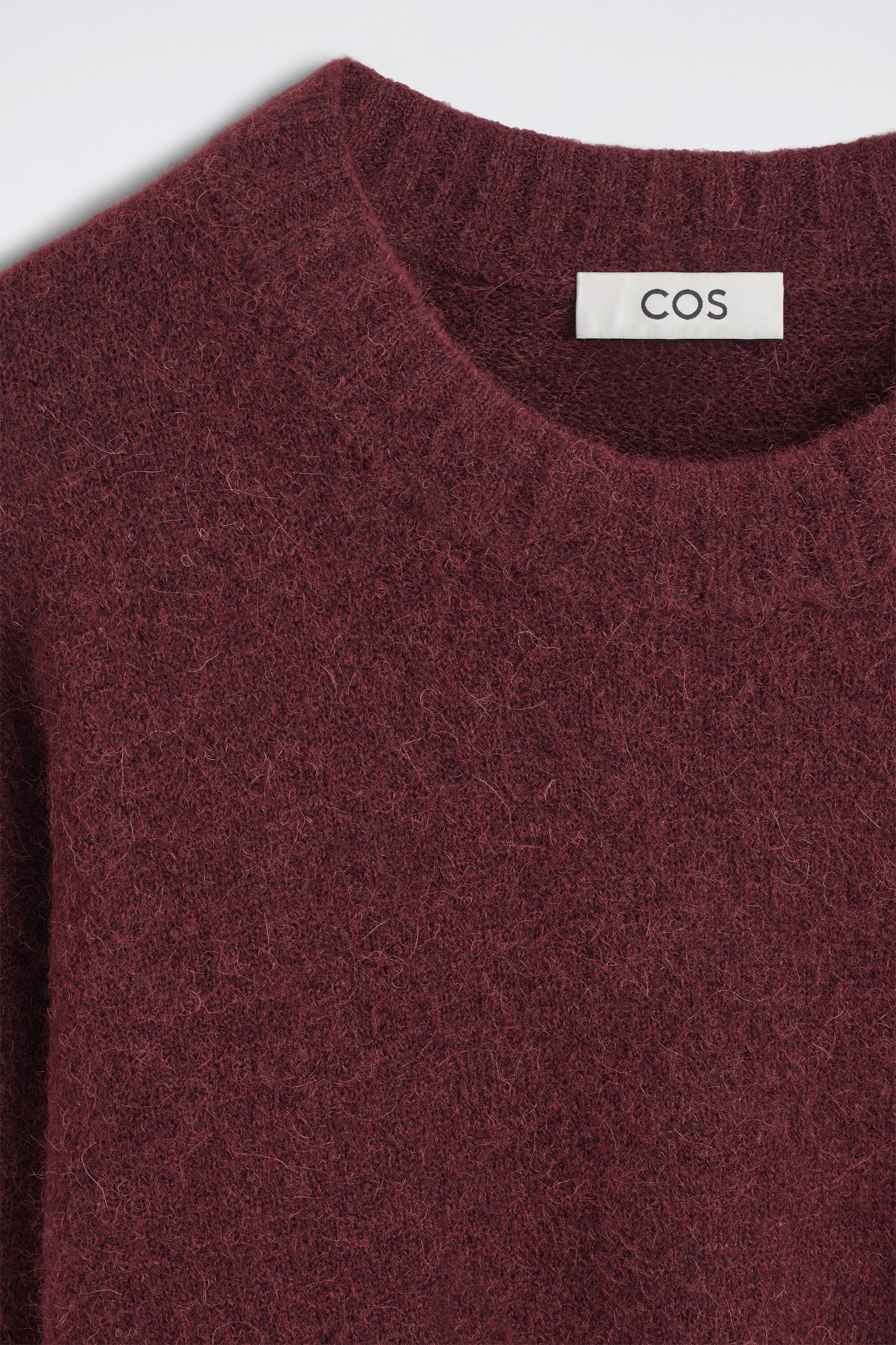 The oversized alpaca-blend crew-neck sweater is shown in a close-up front view, highlighting its fuzzy, textured knit in a deep burgundy colour. The ribbed crew neckline displays a white sewn-in brand label. The oversized alpaca-blend crew-neck sweater is shown in a close-up front view, highlighting its fuzzy, textured knit in a deep burgundy colour. The ribbed crew neckline displays a white sewn-in brand label.