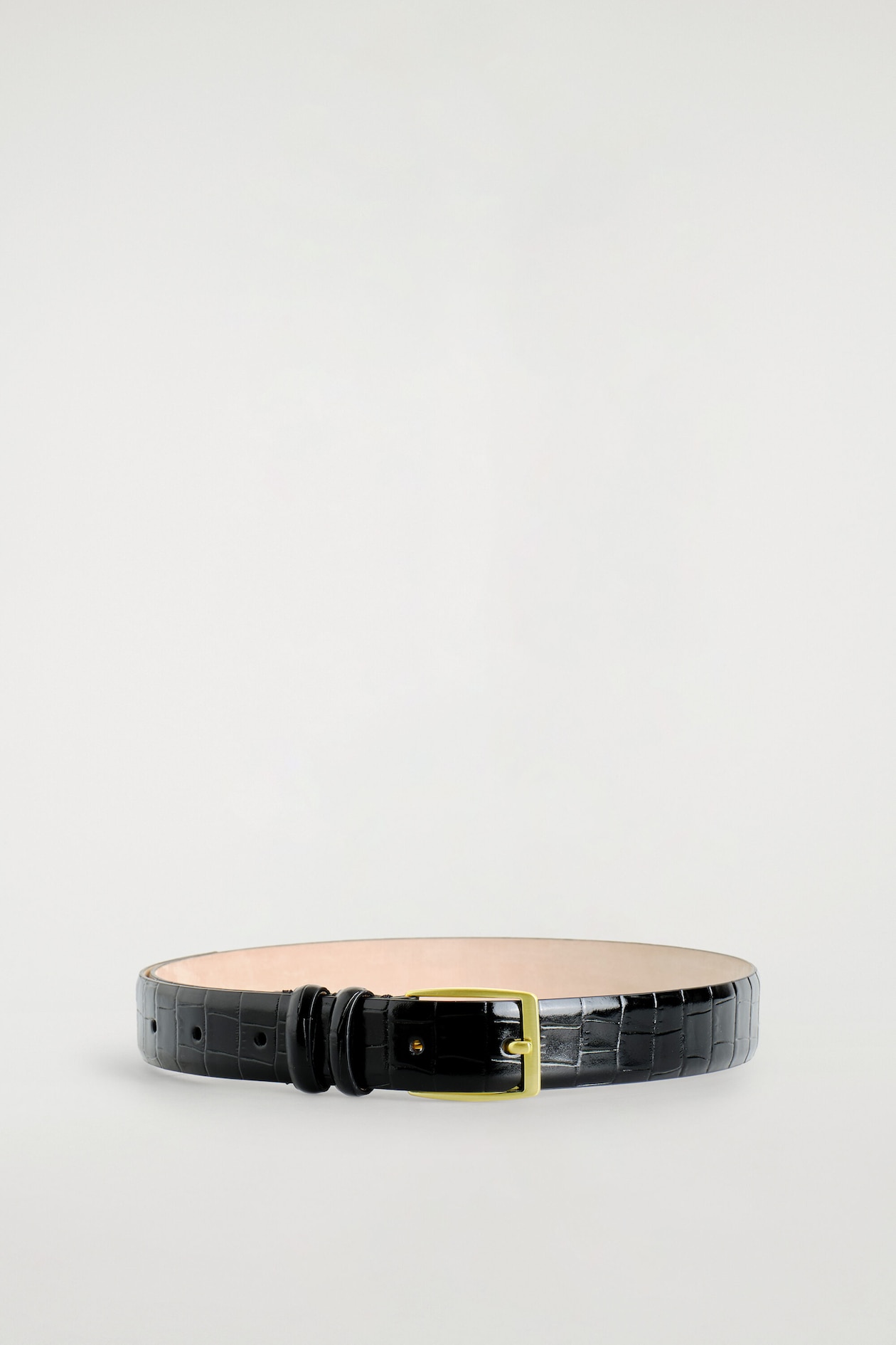 A black croc-effect leather belt is arranged in a coiled, circular position facing front. The belt features a glossy, croc-embossed texture, a rectangular gold-toned buckle, dual matching leather keepers, and a contrasting light beige interior.