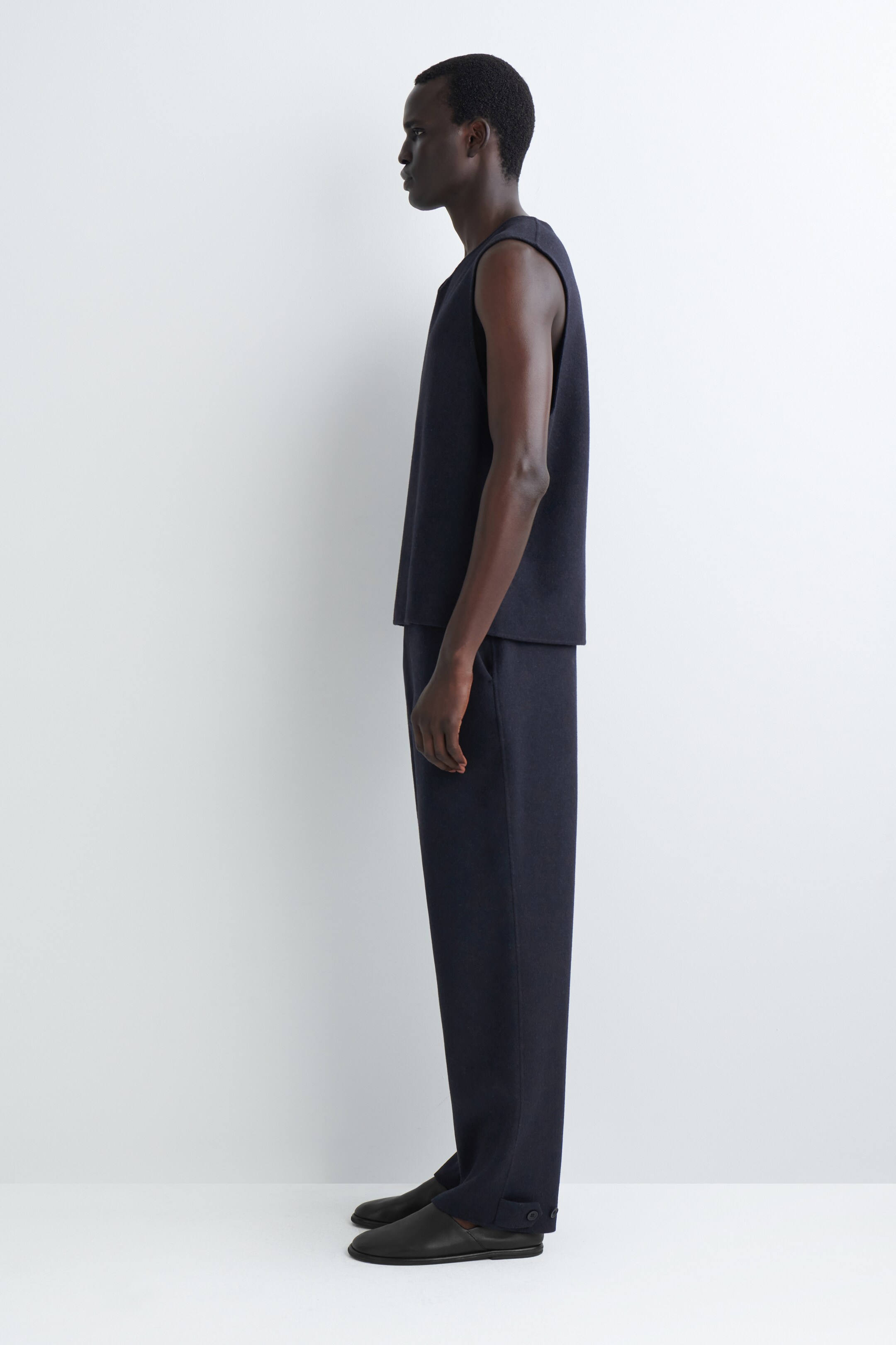 Agrandir l'image: Un haut sans manches bleu foncé et un pantalon assorti sont présentés en vue de profil. Le haut présente une coupe droite et une encolure ronde, tandis que le pantalon montre une jambe droite et décontractée avec des détails de boutons visibles près de la cheville.