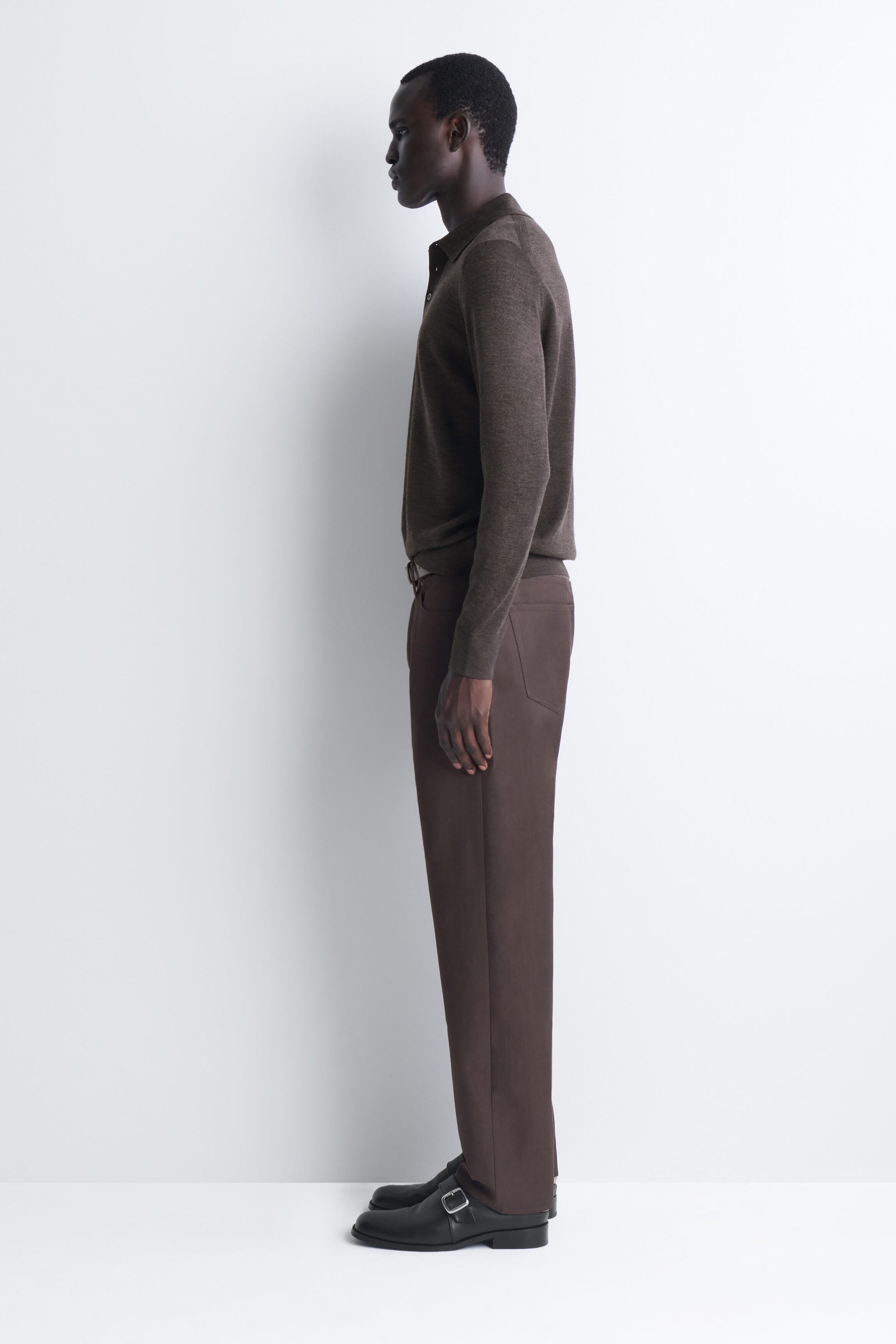 The signature regular-fit straight-leg jeans in dark brown are worn in a side profile facing left, highlighting their straight-cut silhouette and classic back pocket. The jeans are styled with a brown long-sleeve polo shirt tucked into the waistband and paired with black leather shoes. The signature regular-fit straight-leg jeans in dark brown are worn in a side profile facing left, highlighting their straight-cut silhouette and classic back pocket. The jeans are styled with a brown long-sleeve polo shirt tucked into the waistband and paired with black leather shoes.