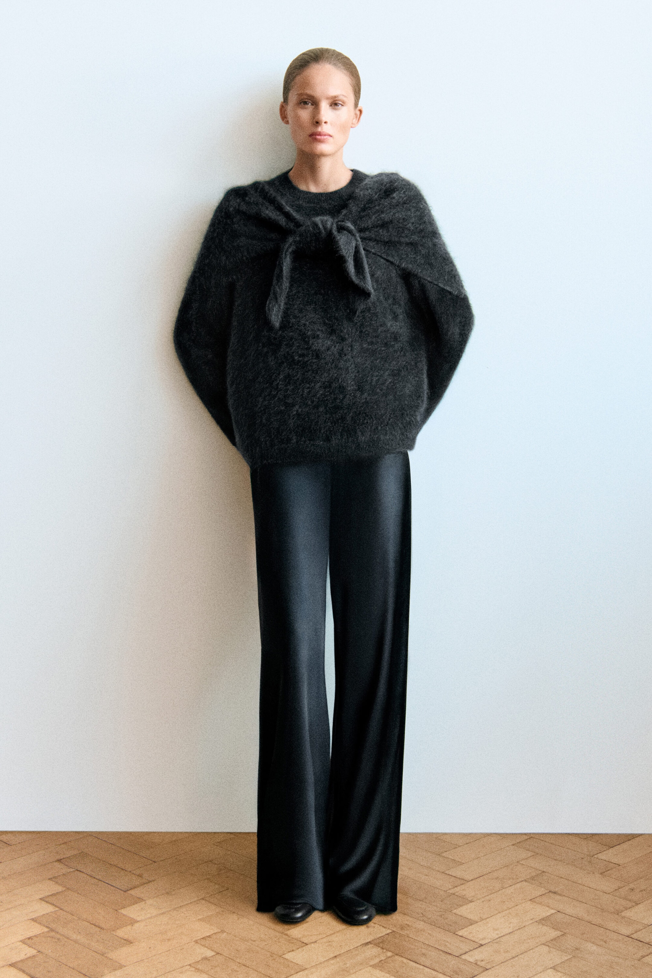 Facing front, a model is wearing a dark-grey, brushed-cashmere crew-neck jumper styled with a matching brushed-cashmere triangle scarf draped and tied around the shoulders. The outfit is completed with black satin wide-leg trousers. Facing front, a model is wearing a dark-grey, brushed-cashmere crew-neck jumper styled with a matching brushed-cashmere triangle scarf draped and tied around the shoulders. The outfit is completed with black satin wide-leg trousers.