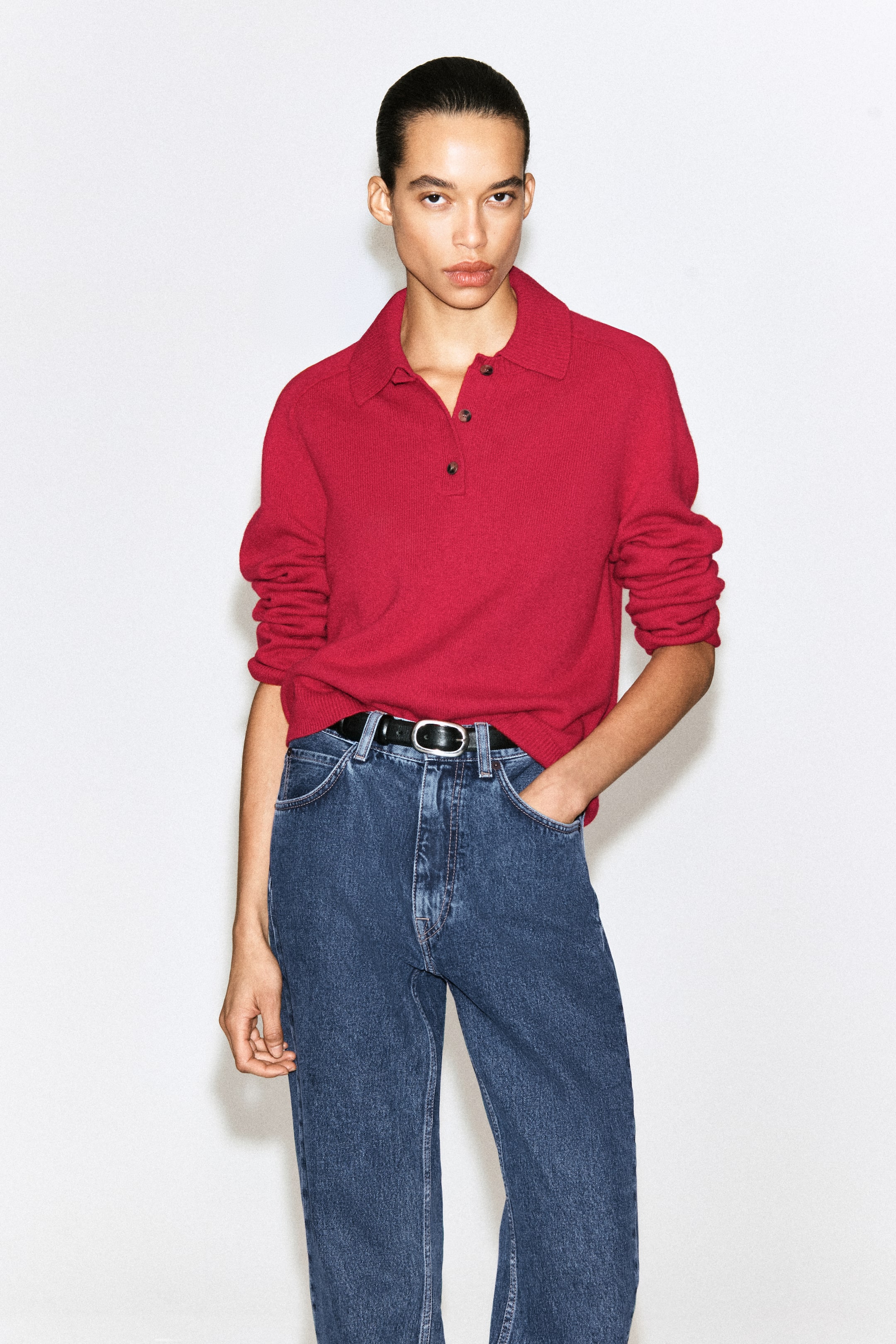 Ver imagen más grande: Se muestra desde el frente un polo de punto rojo, con cuello acanalado, una tapeta de tres botones con botones oscuros y mangas largas con puños acanalados. La camisa tiene un corte regular y el bajo está parcialmente remetido.