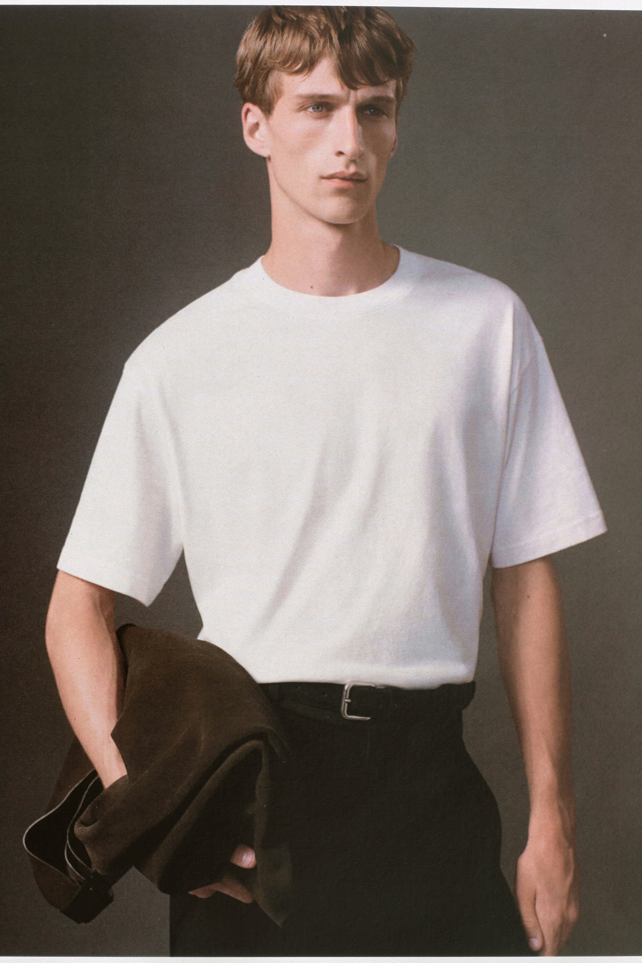 Visa större bild: En vit T-shirt med rund hals bärs framifrån, med en avslappnad passform med nedhasade axlar och korta ärmar. T-shirten är för närvarande instoppad i svarta byxor.