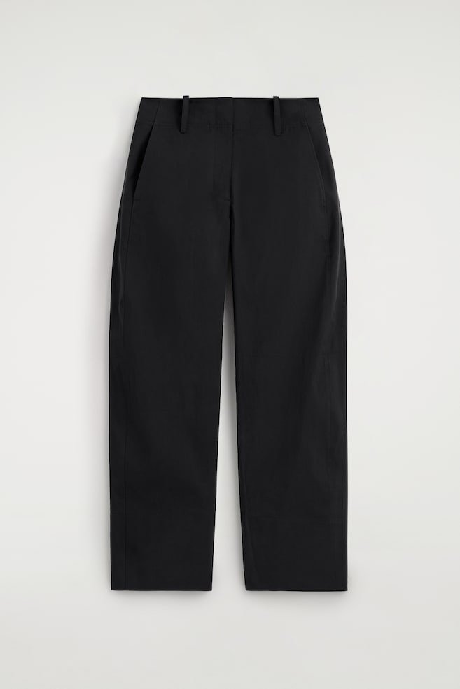 Pantalones negros de pierna barril se muestran de frente. Presentan una silueta limpia en un tejido nítido, con trabillas de cinturón sobredimensionadas en la cintura y discretos bolsillos laterales. - 1