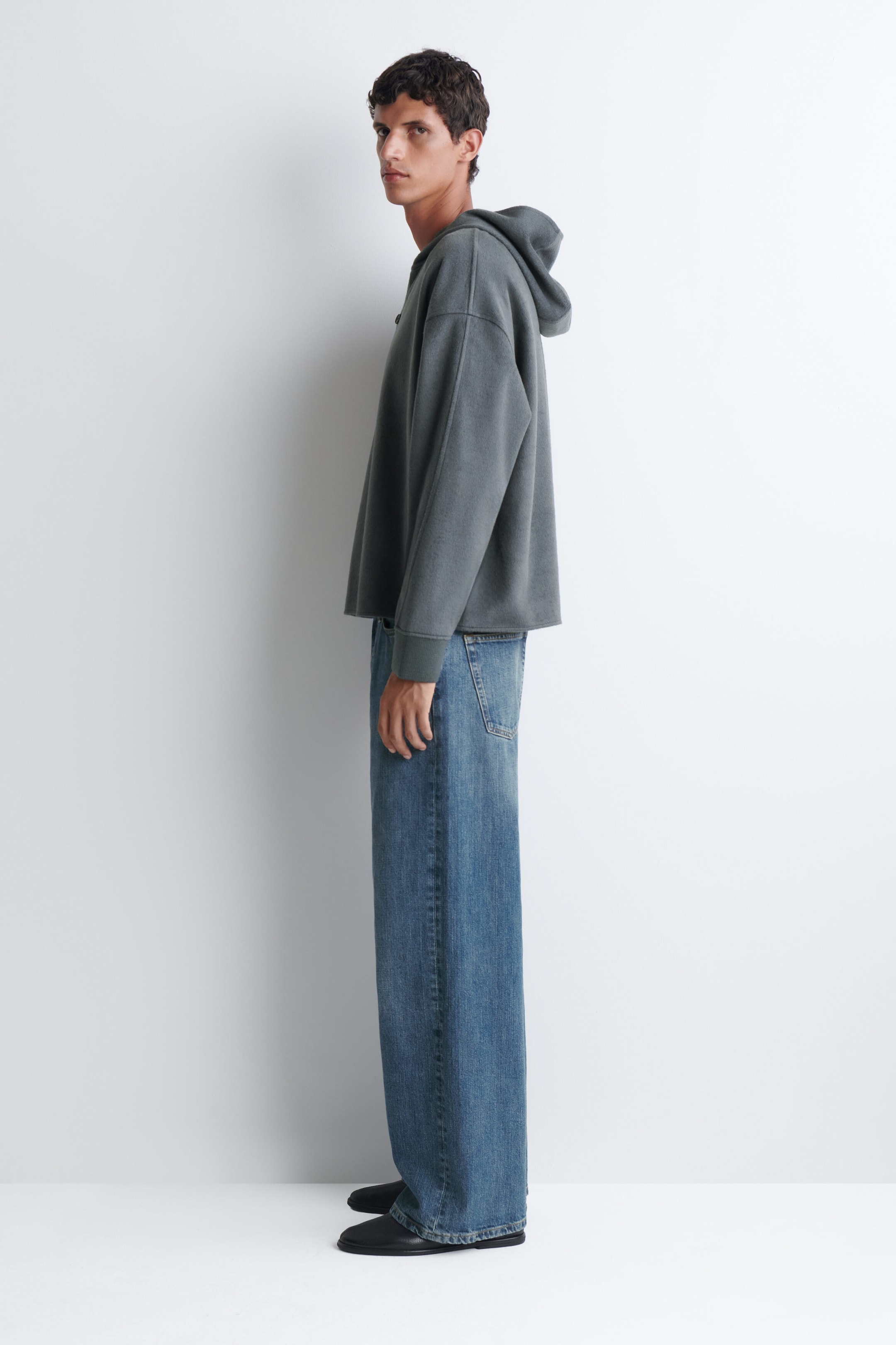 Un chandail à capuchon gris foncé à coupe décontractée et épaules tombantes est porté par le mannequin, agencé à un jean bleu à jambe large. Un chandail à capuchon gris foncé à coupe décontractée et épaules tombantes est porté par le mannequin, agencé à un jean bleu à jambe large.