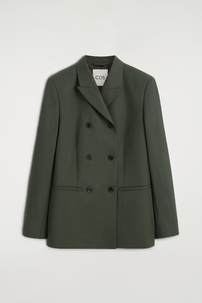 Een donkergroene double-breasted blazer is van voren te zien, met scherpe revers met inkeping, gestructureerde schouders en een sluiting met zes knopen. De blazer heeft een getailleerd silhouet, gevormd door taillenaden, en is voorzien van twee horizontale paspelzakken. - 1
