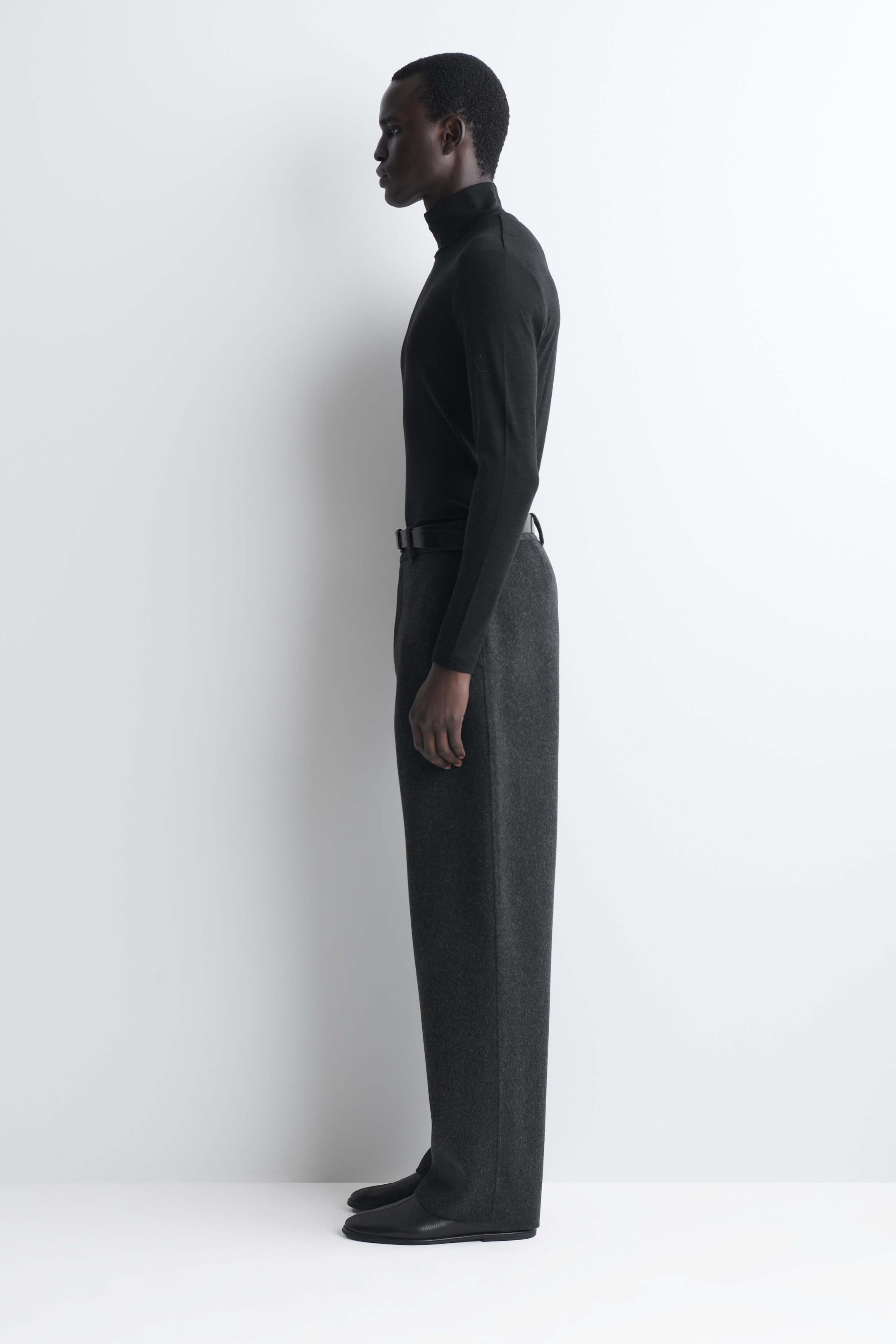 The black slim wool jersey roll-neck top features a fitted, long-sleeved silhouette with a high, structured collar, presented in side profile facing left. The lightweight top is worn tucked into dark trousers, highlighting its slim, streamlined fit. The black slim wool jersey roll-neck top features a fitted, long-sleeved silhouette with a high, structured collar, presented in side profile facing left. The lightweight top is worn tucked into dark trousers, highlighting its slim, streamlined fit.