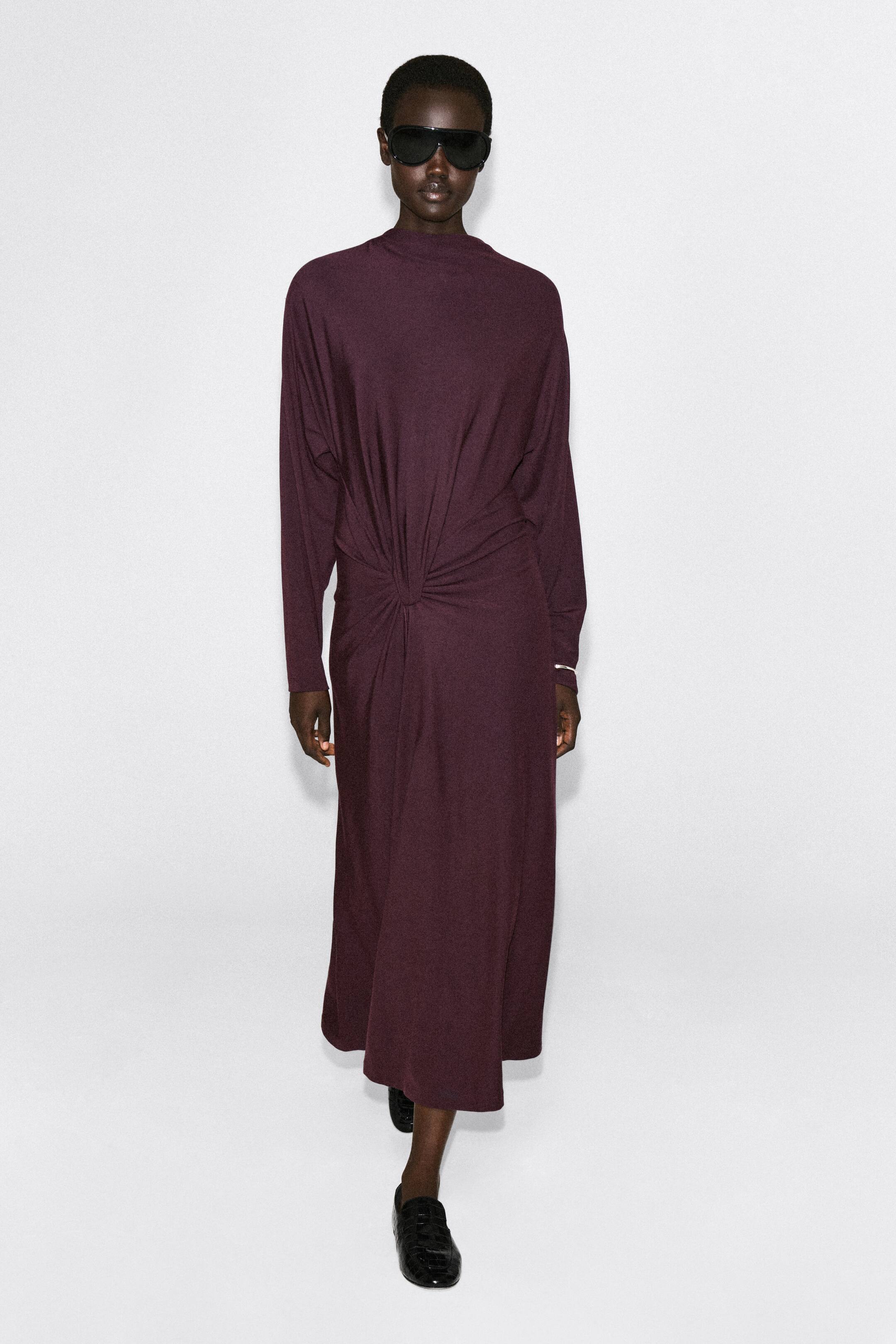 Agrandir l'image: Une robe midi drapée couleur prune foncée est présentée de face, avec un col montant et des manches longues. Un détail torsadé bien visible à la taille crée de doux plis drapés qui rayonnent sur le buste et se prolongent sur la jupe mi-longue.