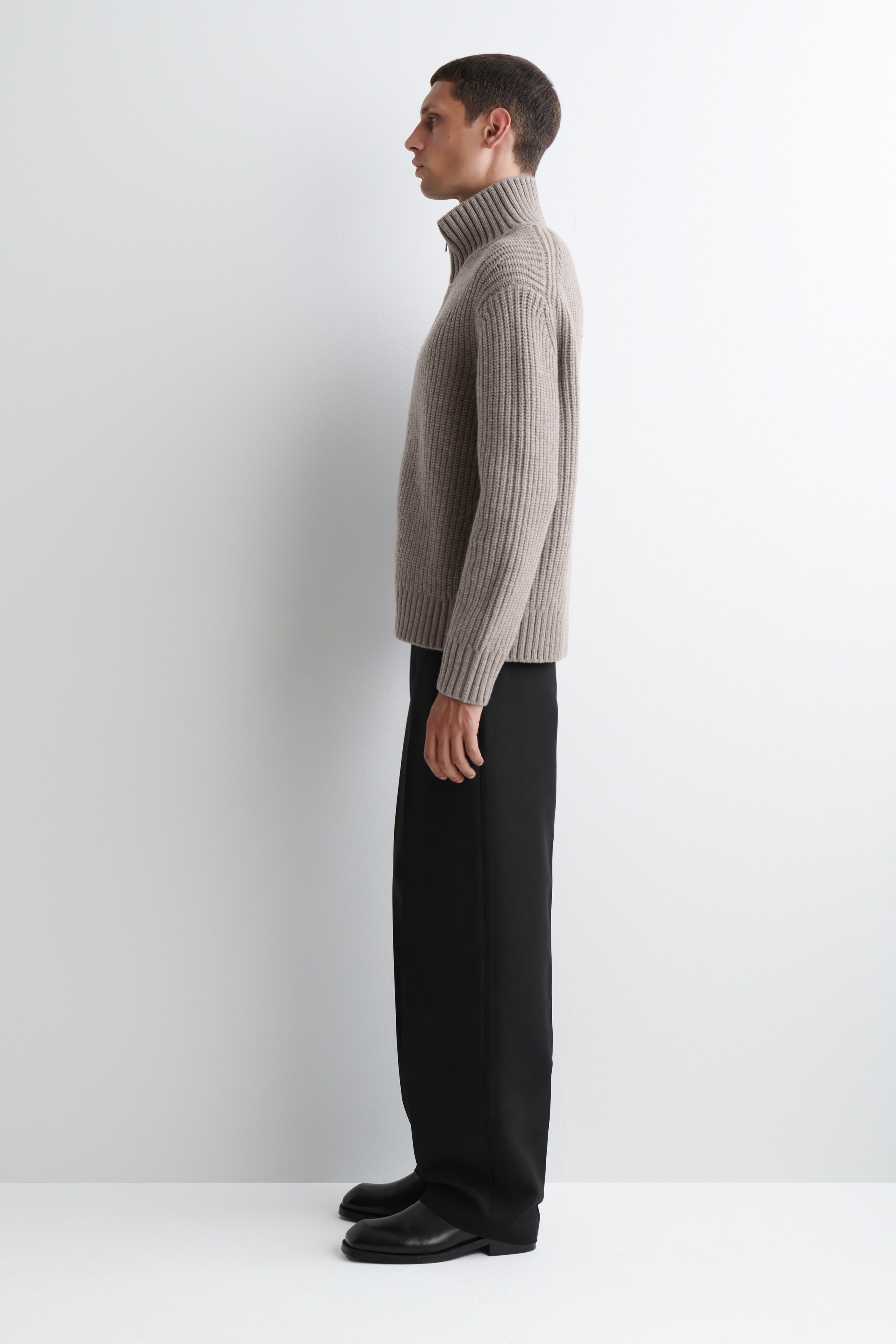 Se større billede: En beige ribbet half-zip sweater præsenteres fra en sideprofil. Den har en høj funnellkrave med en synlig lynlåstræk, lange ribbede ærmer og en ribbet kant samt manchetter.