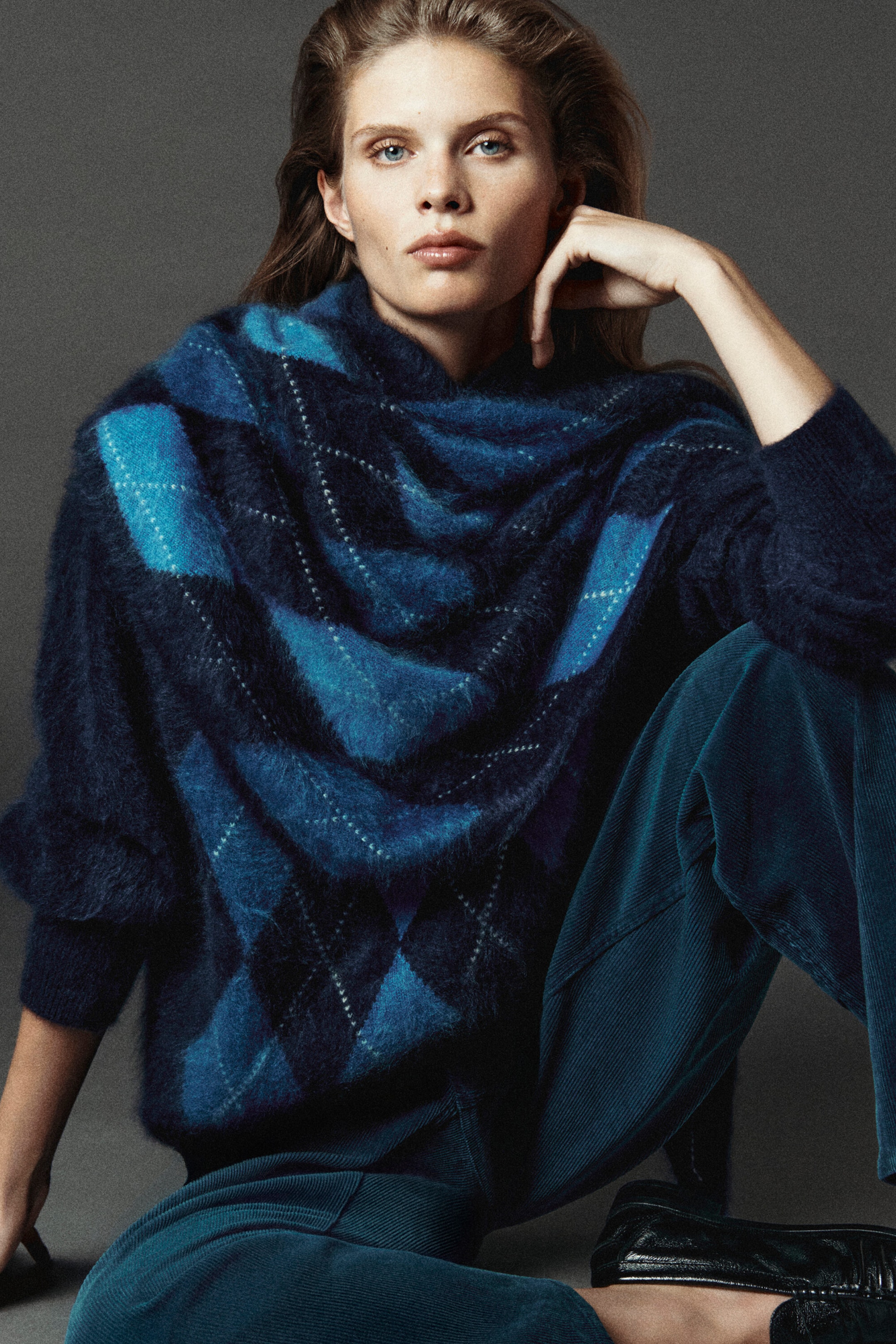 This brushed cashmere funnel neck jumper and matching triangular scarf feature a fuzzy, textured knit in a blue argyle pattern. The front-facing model is wearing the scarf draped over the shoulders of the relaxed-fit jumper, which is styled with dark blue corduroy trousers. This brushed cashmere funnel neck jumper and matching triangular scarf feature a fuzzy, textured knit in a blue argyle pattern. The front-facing model is wearing the scarf draped over the shoulders of the relaxed-fit jumper, which is styled with dark blue corduroy trousers.