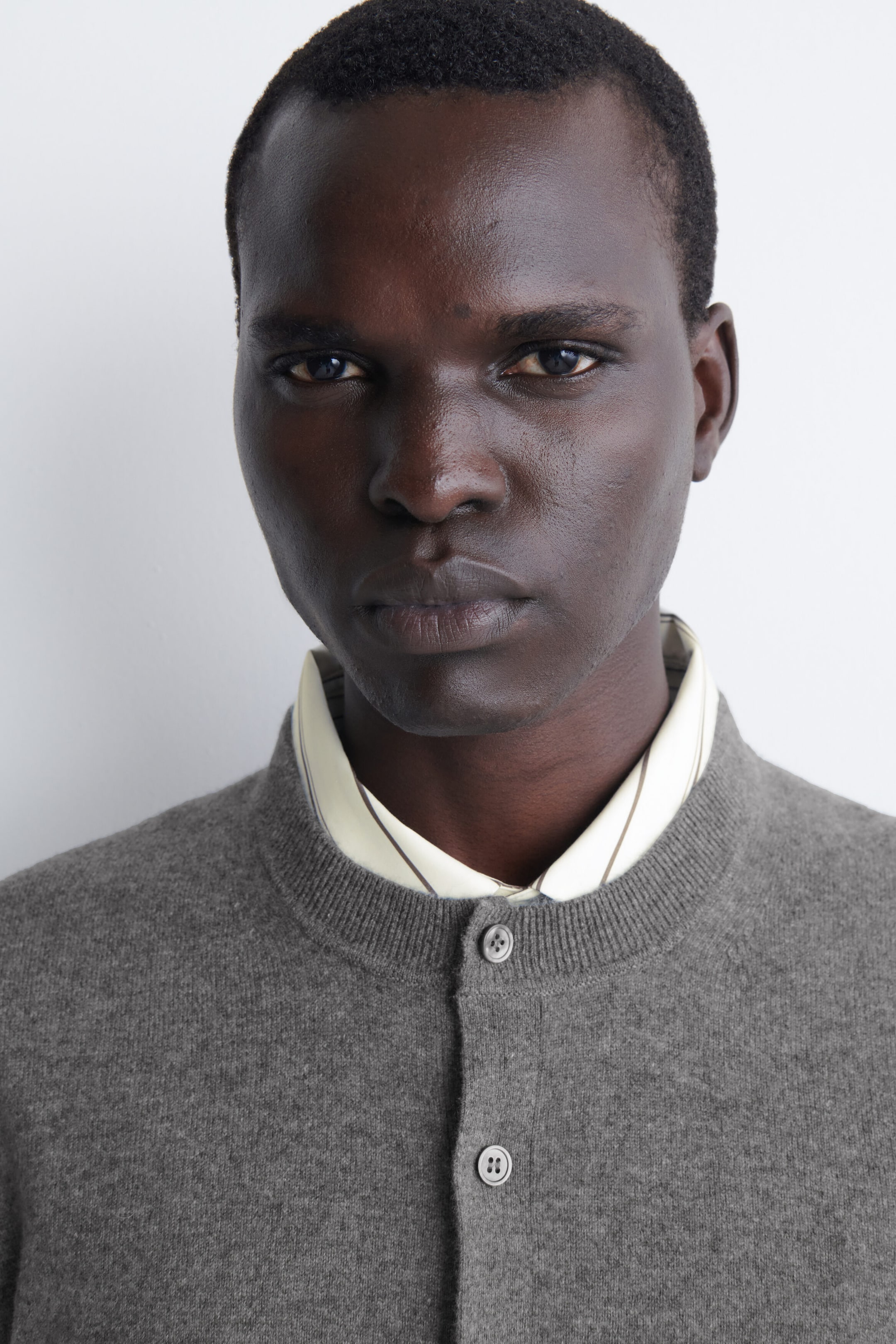 Un cardigan en cachemire gris est porté par-dessus une chemise claire à col, mettant en valeur sa maille fine et son col rond côtelé. La partie supérieure du cardigan montre deux boutons de fermeture sur l’avant. Un cardigan en cachemire gris est porté par-dessus une chemise claire à col, mettant en valeur sa maille fine et son col rond côtelé. La partie supérieure du cardigan montre deux boutons de fermeture sur l’avant.