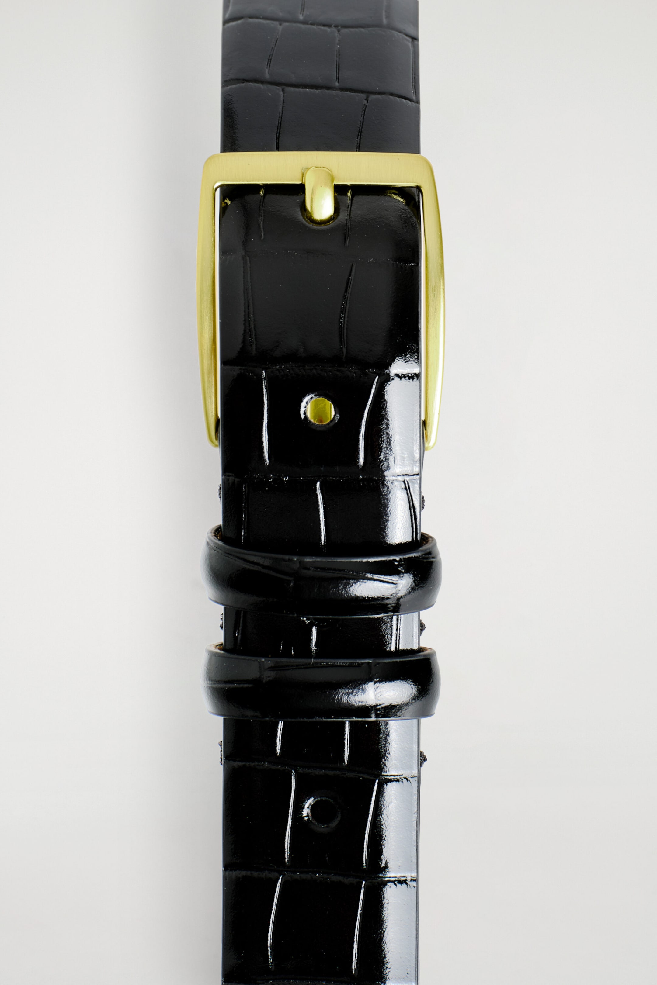 A croc-effect leather belt is displaying a glossy black crocodile-embossed texture in a front close-up view. The belt is featuring a rectangular gold-toned buckle with a single prong and two matching leather keeper loops.