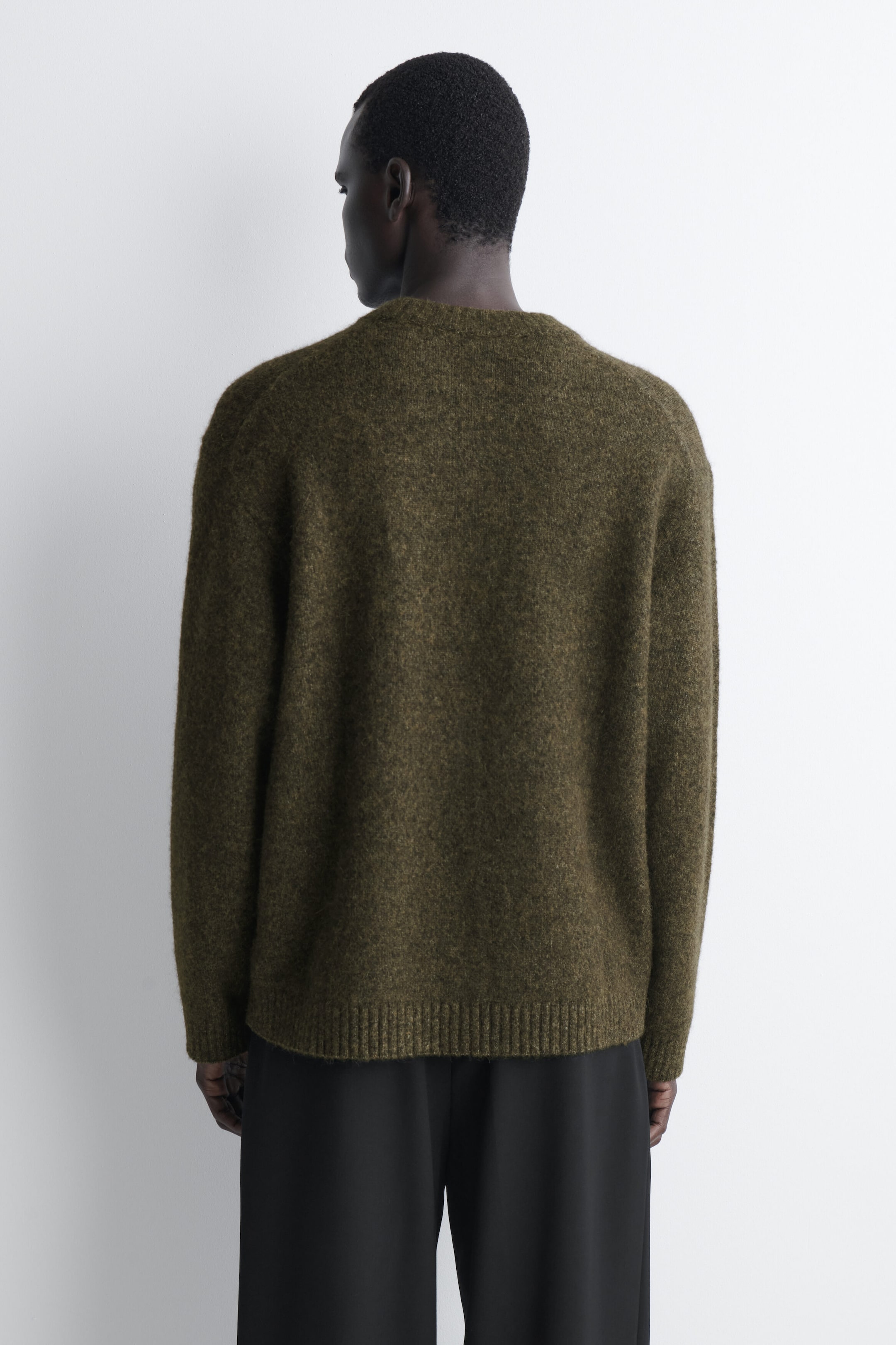 The oversized alpaca-blend crew-neck jumper is shown from the back, highlighting its relaxed fit and textured, fuzzy olive-green knit. It is styled with black trousers, which sit beneath the jumper's ribbed hem. The oversized alpaca-blend crew-neck jumper is shown from the back, highlighting its relaxed fit and textured, fuzzy olive-green knit. It is styled with black trousers, which sit beneath the jumper's ribbed hem.