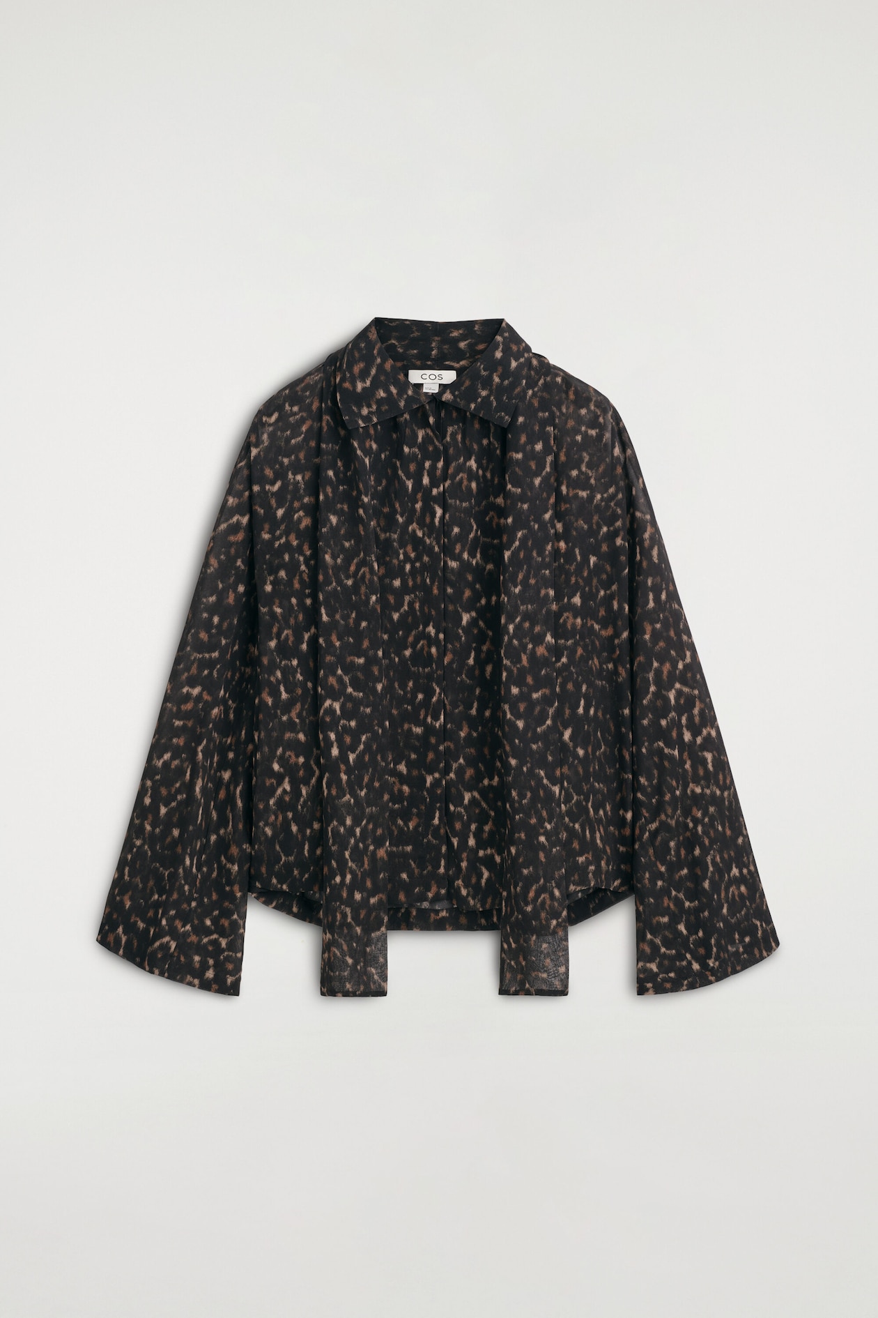 The leopard-print fluid scarf-detail top is shown from the front, featuring a relaxed silhouette with wide, flared long sleeves and a pointed collar. Two matching fabric panels hang down from the neckline, creating a draped, scarf-like detail over the concealed front placket.