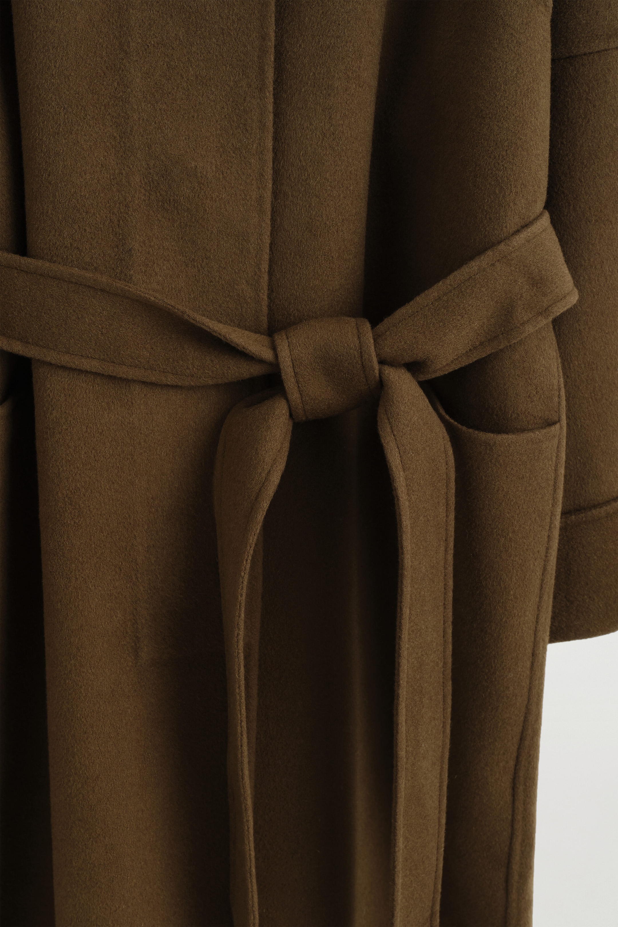 A brown wool-blend coat is shown from the front, featuring a matching fabric belt tied in a knot at the waist. The coat showcases a soft, textured fabric, with a side pocket visible on the right. A brown wool-blend coat is shown from the front, featuring a matching fabric belt tied in a knot at the waist. The coat showcases a soft, textured fabric, with a side pocket visible on the right.