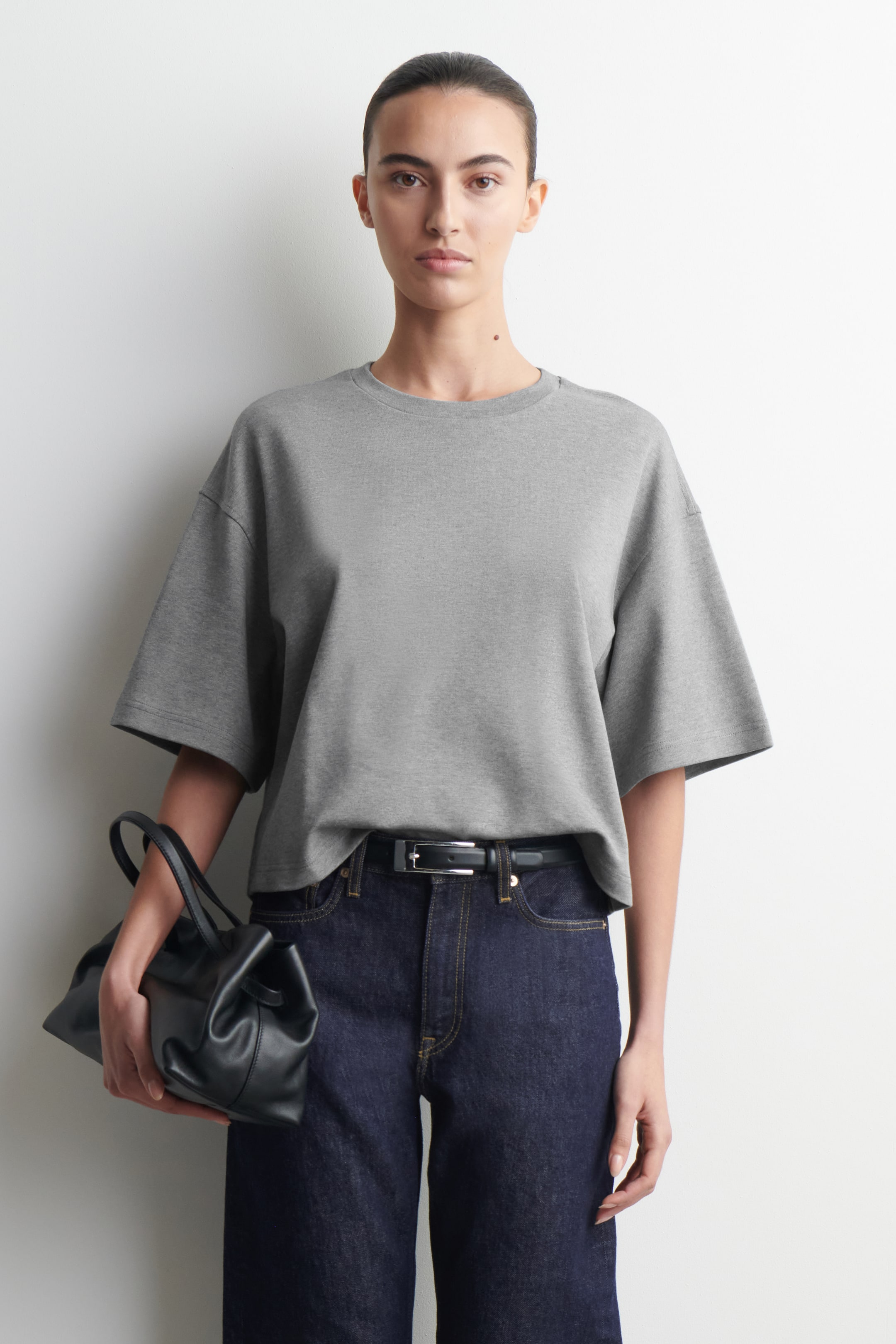 Größeres Bild anzeigen: Ein graues, übergroßes T-Shirt mit geripptem Rundhalsausschnitt und tief angesetzten Ärmeln wird vom Model getragen. Das T-Shirt ist in dunkle Jeans und einen schwarzen Gürtel gesteckt.