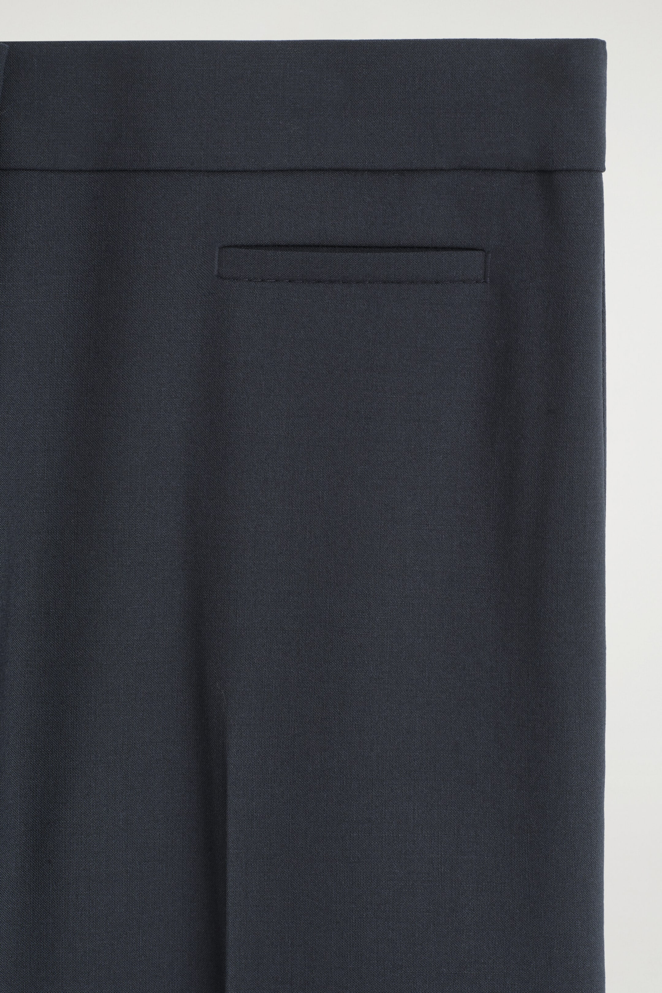 Twill cropped flared pants are shown in a close-up detail view, highlighting the clean-cut waistband and a single horizontal welt pocket on the dark navy blue fabric.