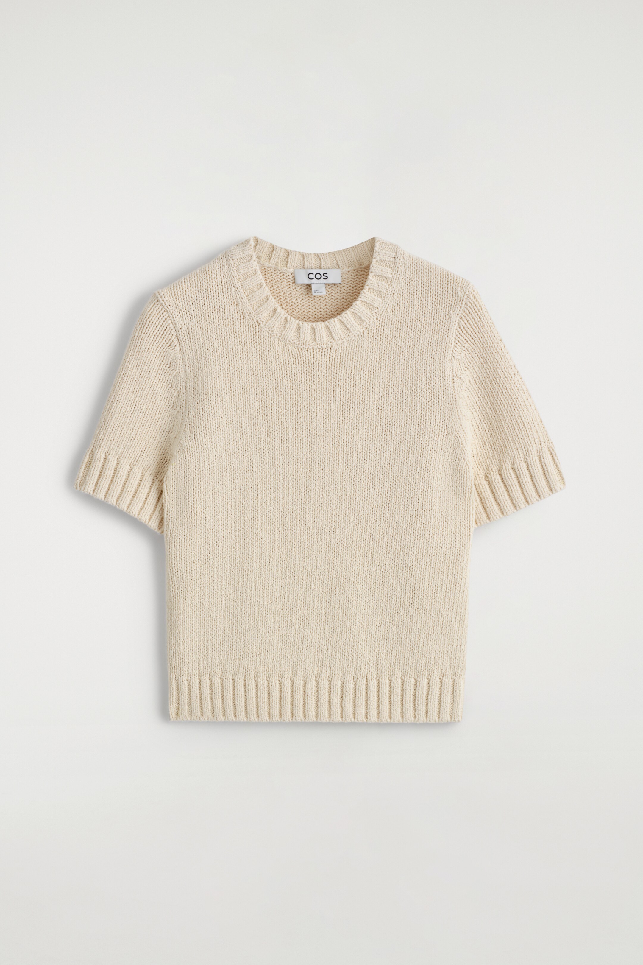 View larger image: An off-white short-sleeved knitted top is lying flat, displaying its front, and is presenting a plain knit body with a ribbed crew neck, ribbed cuffs on the short sleeves, and a ribbed hem. A 'COS' tag is showing inside the neckline.