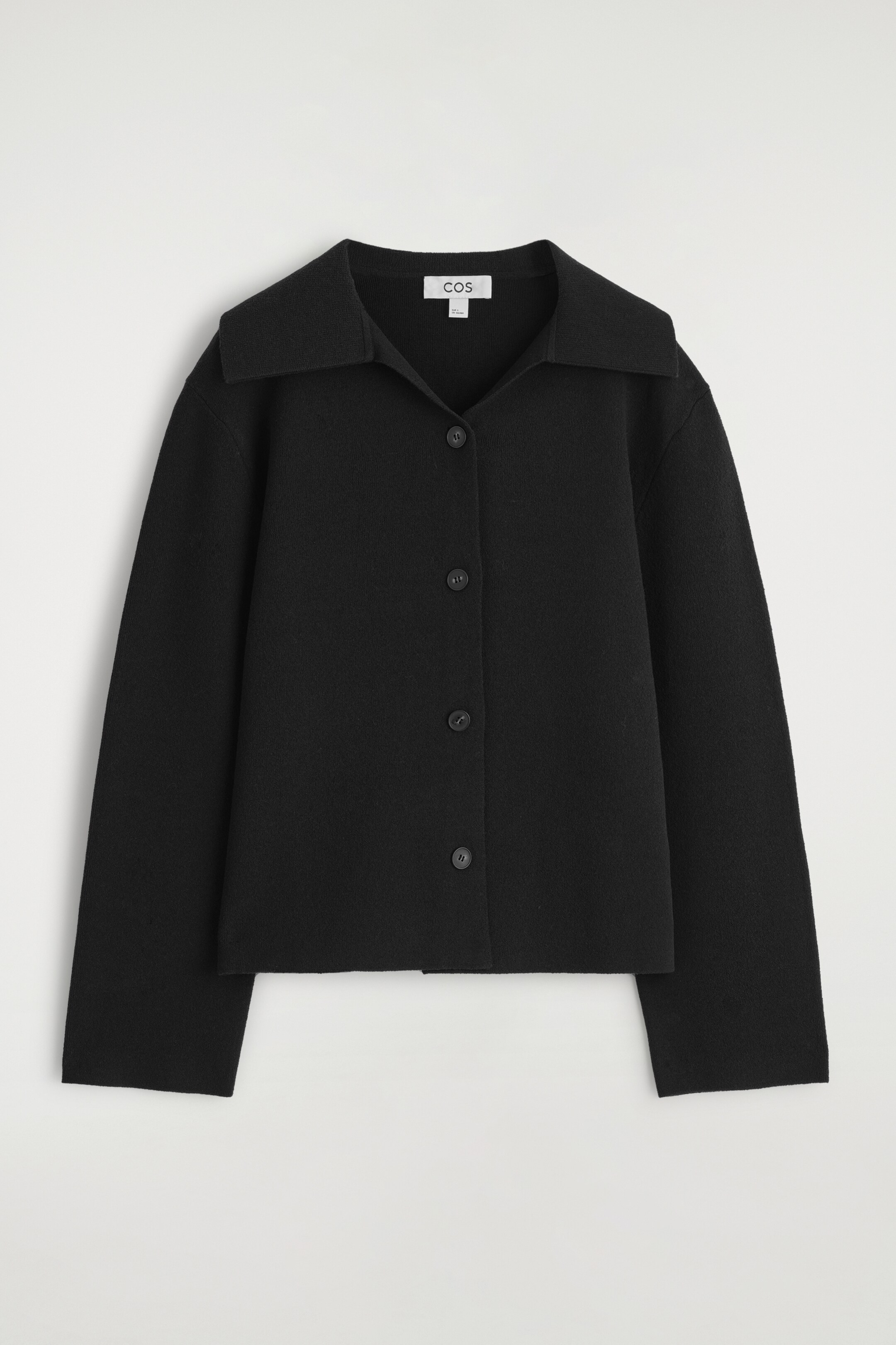 Größeres Bild anzeigen: Eine schwarze Strickjacke wird VORNE präsentiert, mit einem weit gespreizten Kragen und einem vierknöpfigen Verschluss vorne. Sie hat eine entspannte, kastige Passform mit langen, geraden Ärmeln.
