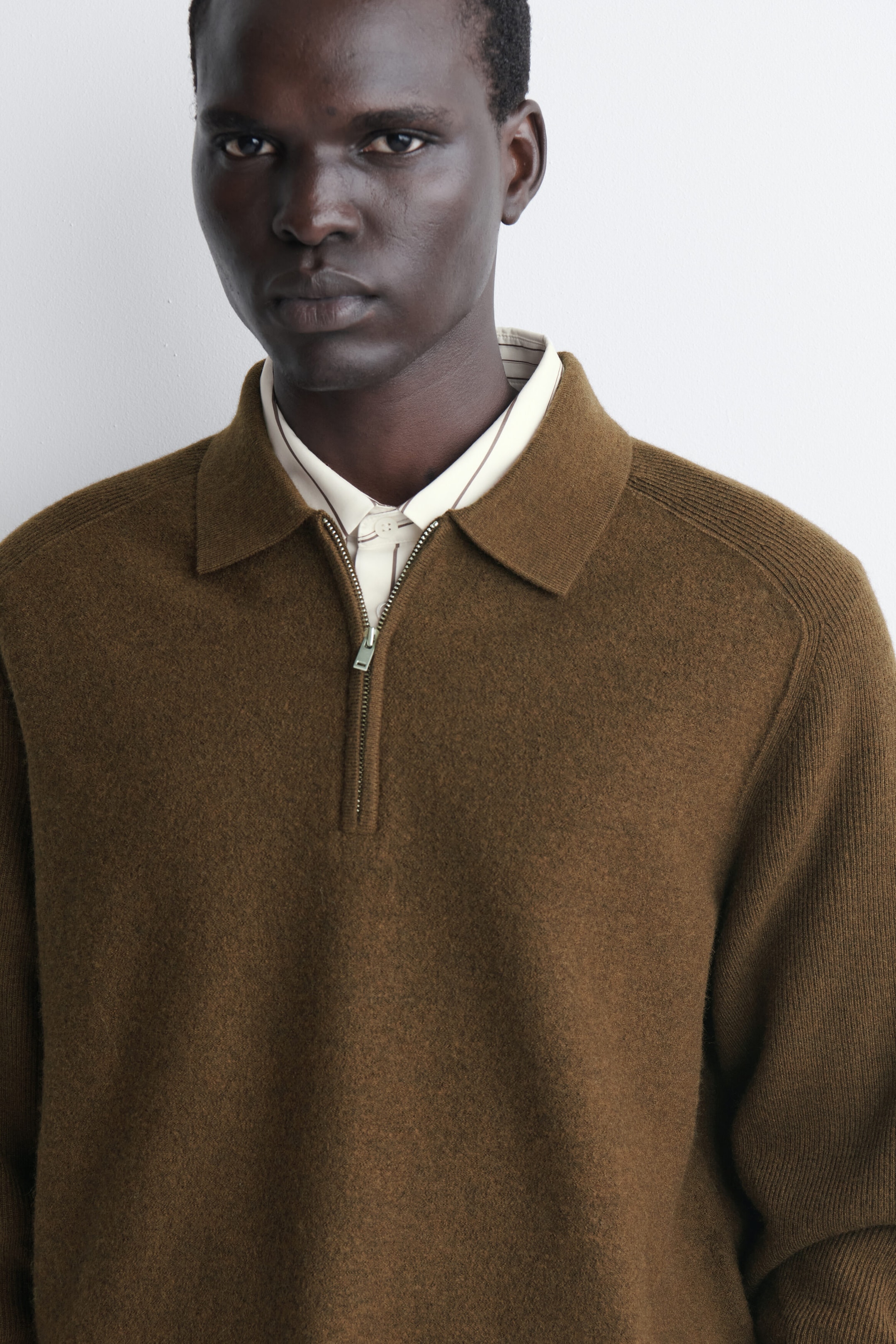 This brown paneled boiled-wool zip-up jumper features a polo collar, a silver-tone half-zip closure, and contrasting ribbed panels along the shoulders and sleeves. It is styled over a light-coloured striped button-down shirt to showcase its textured finish and relaxed fit from a front-facing angle. This brown paneled boiled-wool zip-up jumper features a polo collar, a silver-tone half-zip closure, and contrasting ribbed panels along the shoulders and sleeves. It is styled over a light-coloured striped button-down shirt to showcase its textured finish and relaxed fit from a front-facing angle.