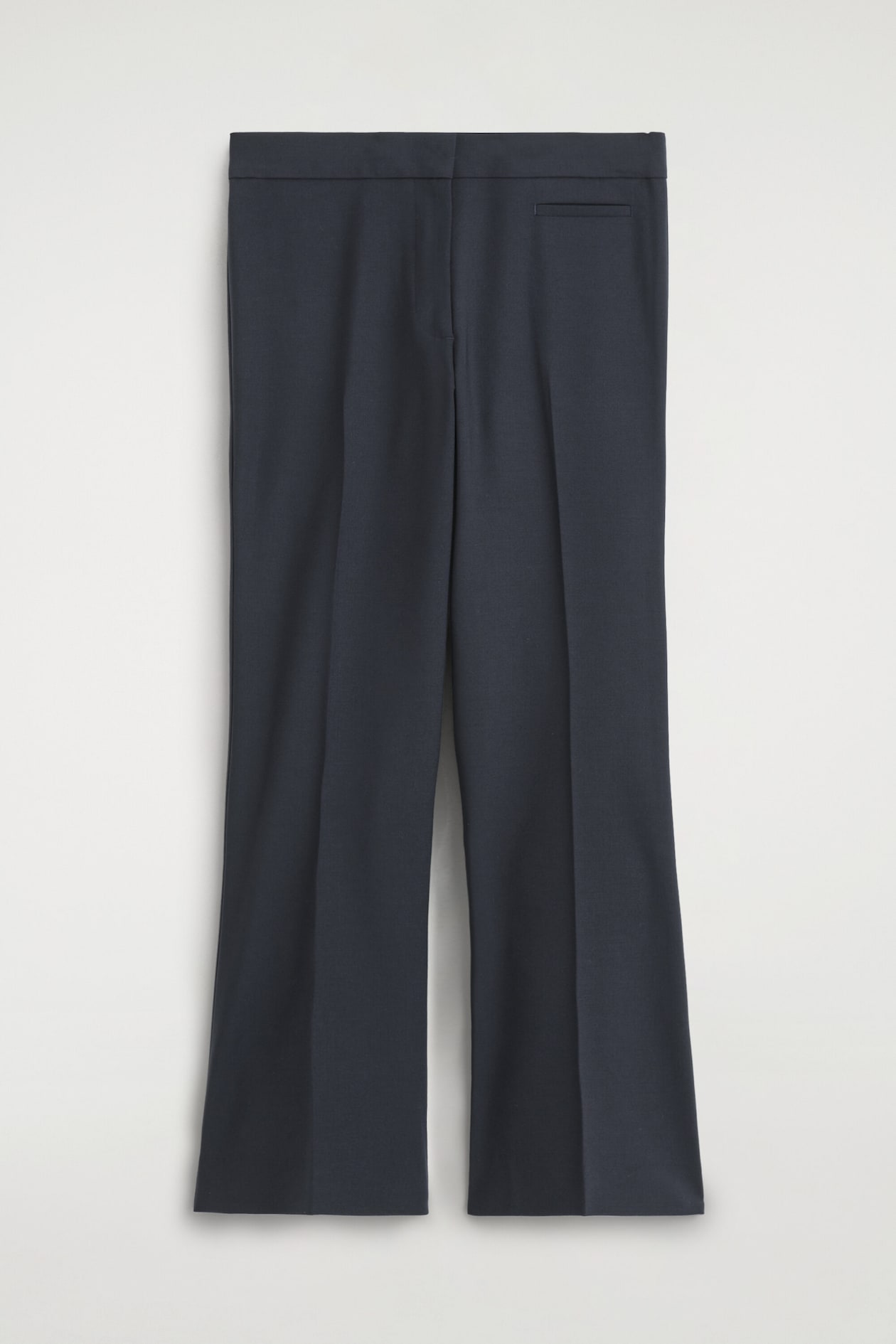 The twill cropped flared pants are shown from the front, displaying a dark navy blue fabric with sharp pressed creases running down the centre of each leg. They feature a structured waistband with a concealed closure, a single welt pocket on the upper right, and a slightly flared hem.