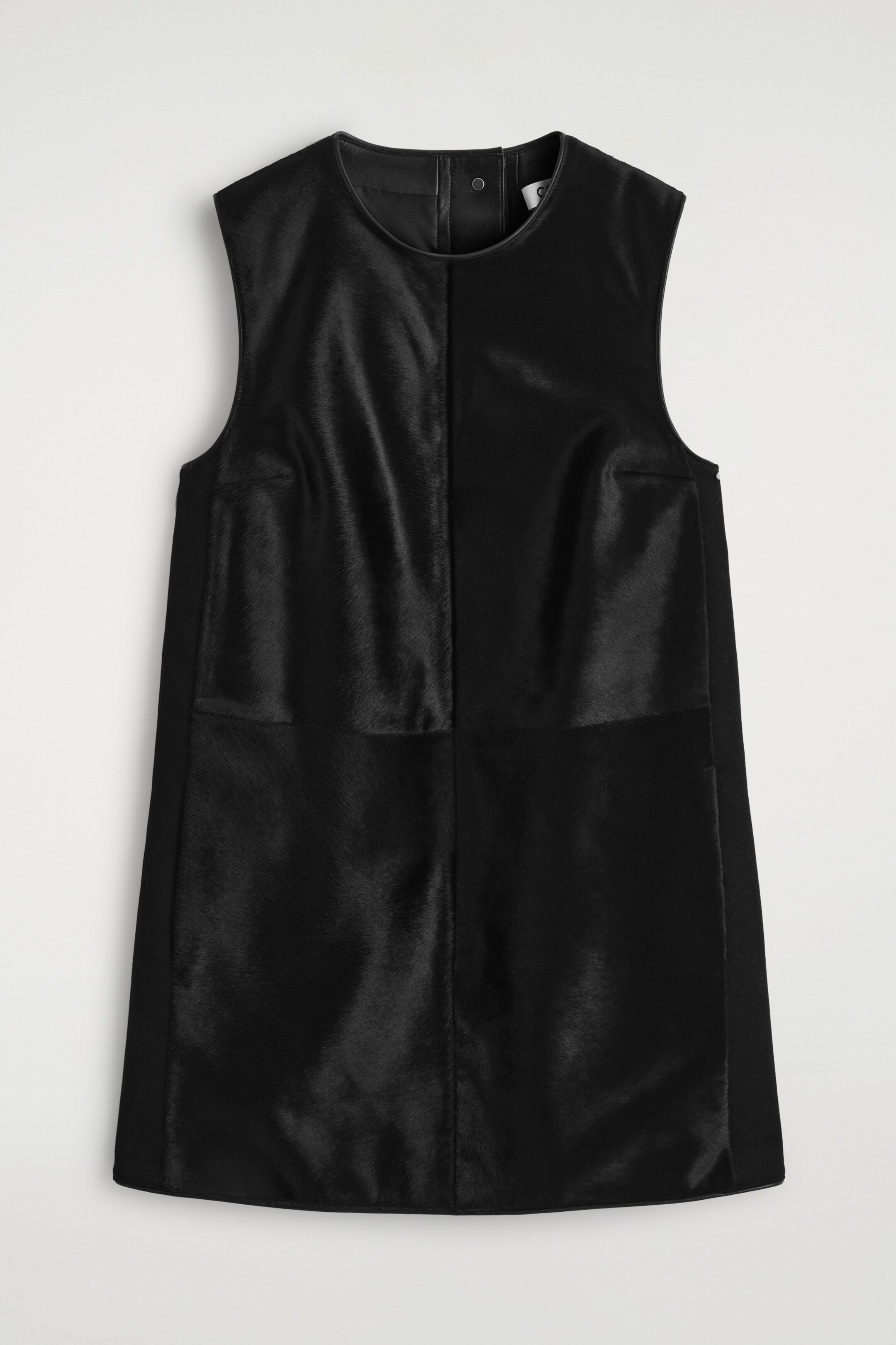 Agrandir l'image: Une robe droite noire sans manches est présentée de FACE, avec un col rond et des panneaux proéminents en cuir à poils de poney contrastant avec du cuir noir lisse sur les panneaux latéraux et la bordure du col, avec une fermeture à pression visible à l'arrière du cou.