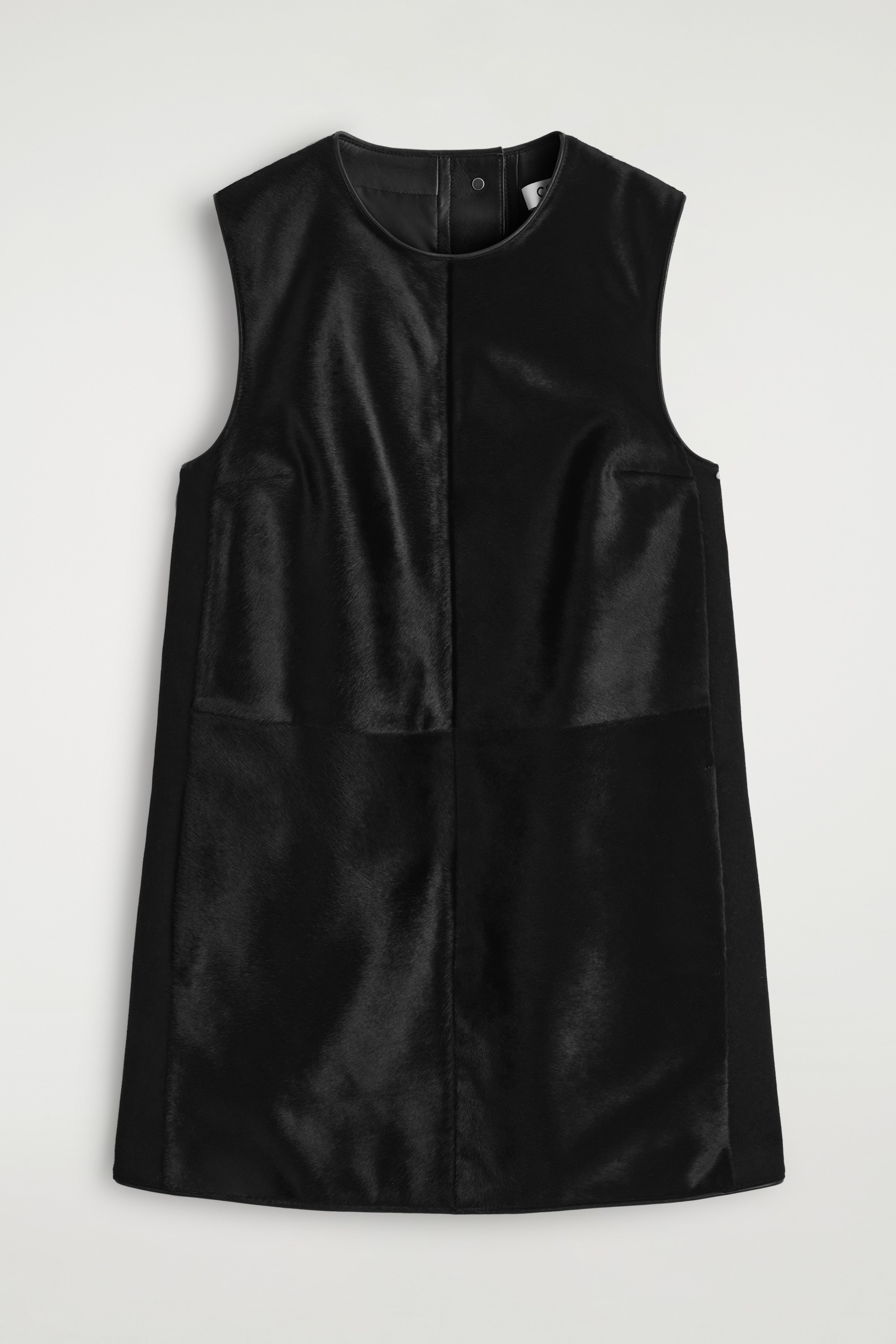 Agrandir l'image: Une robe droite noire sans manches est présentée de FACE, avec un col rond et des panneaux proéminents en cuir à poils de poney contrastant avec du cuir noir lisse sur les panneaux latéraux et la bordure du col, avec une fermeture à pression visible à l'arrière du cou.