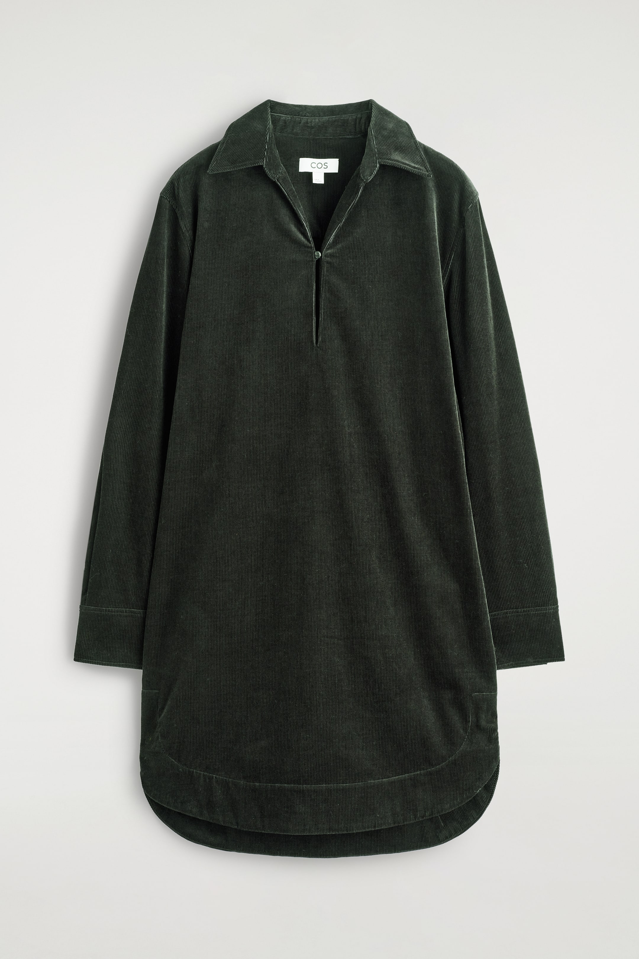 Visualizza immagine più grande: Un vestito a camicia in velluto a coste verde scuro è mostrato frontalmente, con un colletto aperto, un'abbottonatura parziale con una chiusura a bottone singolo, maniche lunghe con polsini abbottonati e un orlo arrotondato.