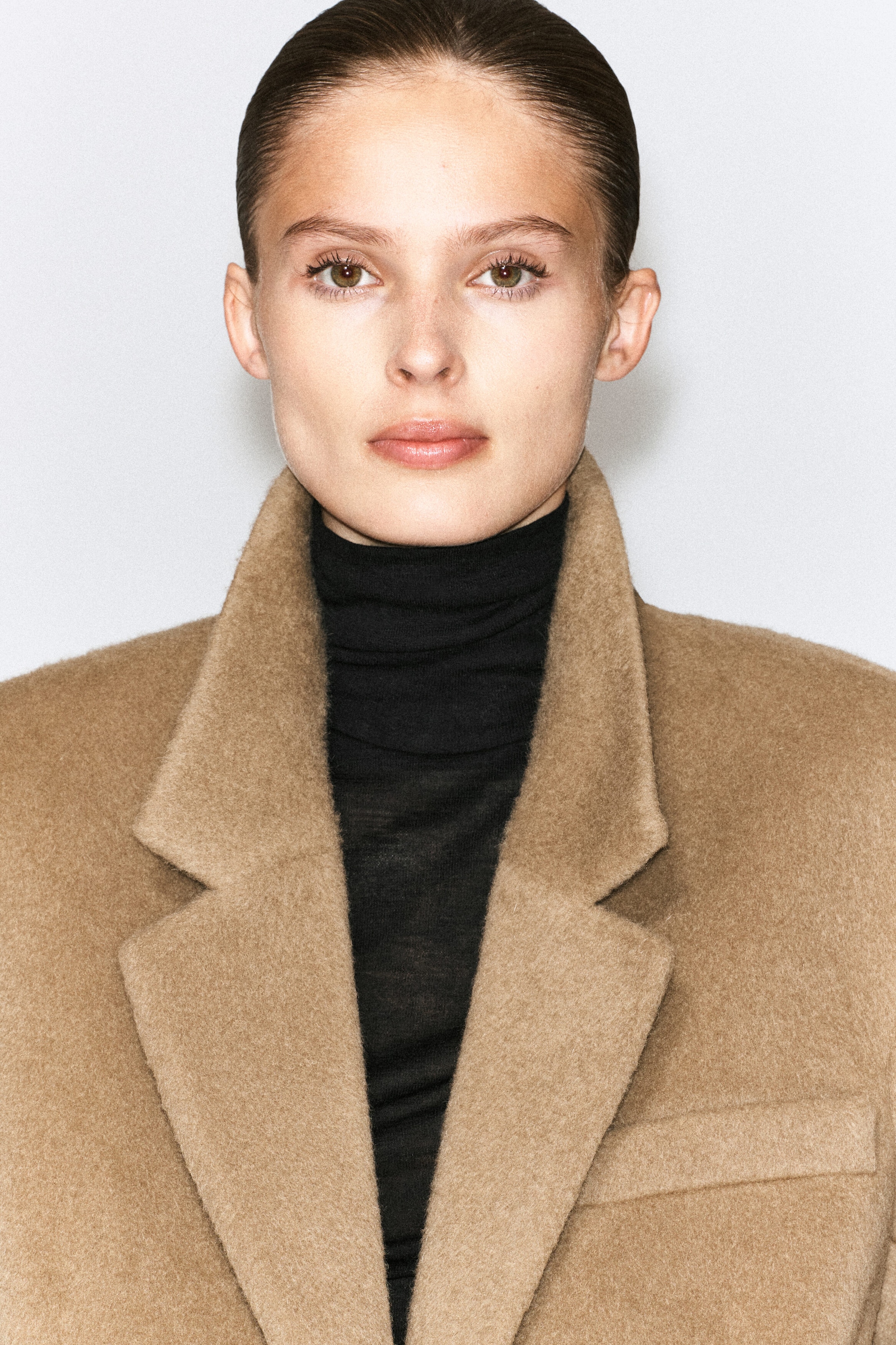 The model is wearing a brushed wool blazer in camel brown over a black turtleneck top. The blazer features wide notched lapels, a soft textured finish, and a chest welt pocket. The model is wearing a brushed wool blazer in camel brown over a black turtleneck top. The blazer features wide notched lapels, a soft textured finish, and a chest welt pocket.