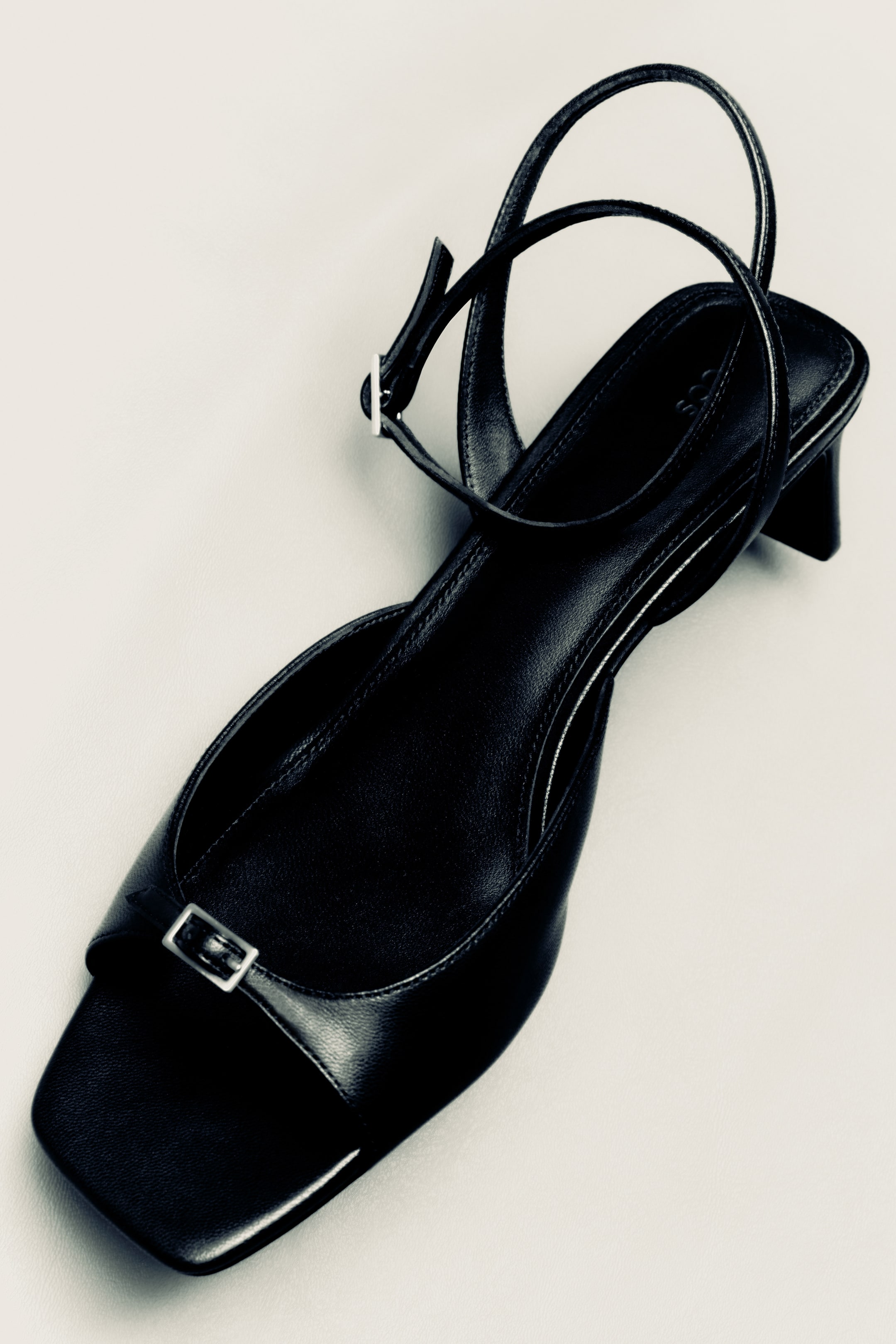 Visa större bild: En svart kitten heel-sko i läder är placerad i en uppifrån-vinkel och visar en fyrkantig tå med ett silvrigt spänne över framdelen. Den har en remdesign med ankelrem och en bred, låg klack.