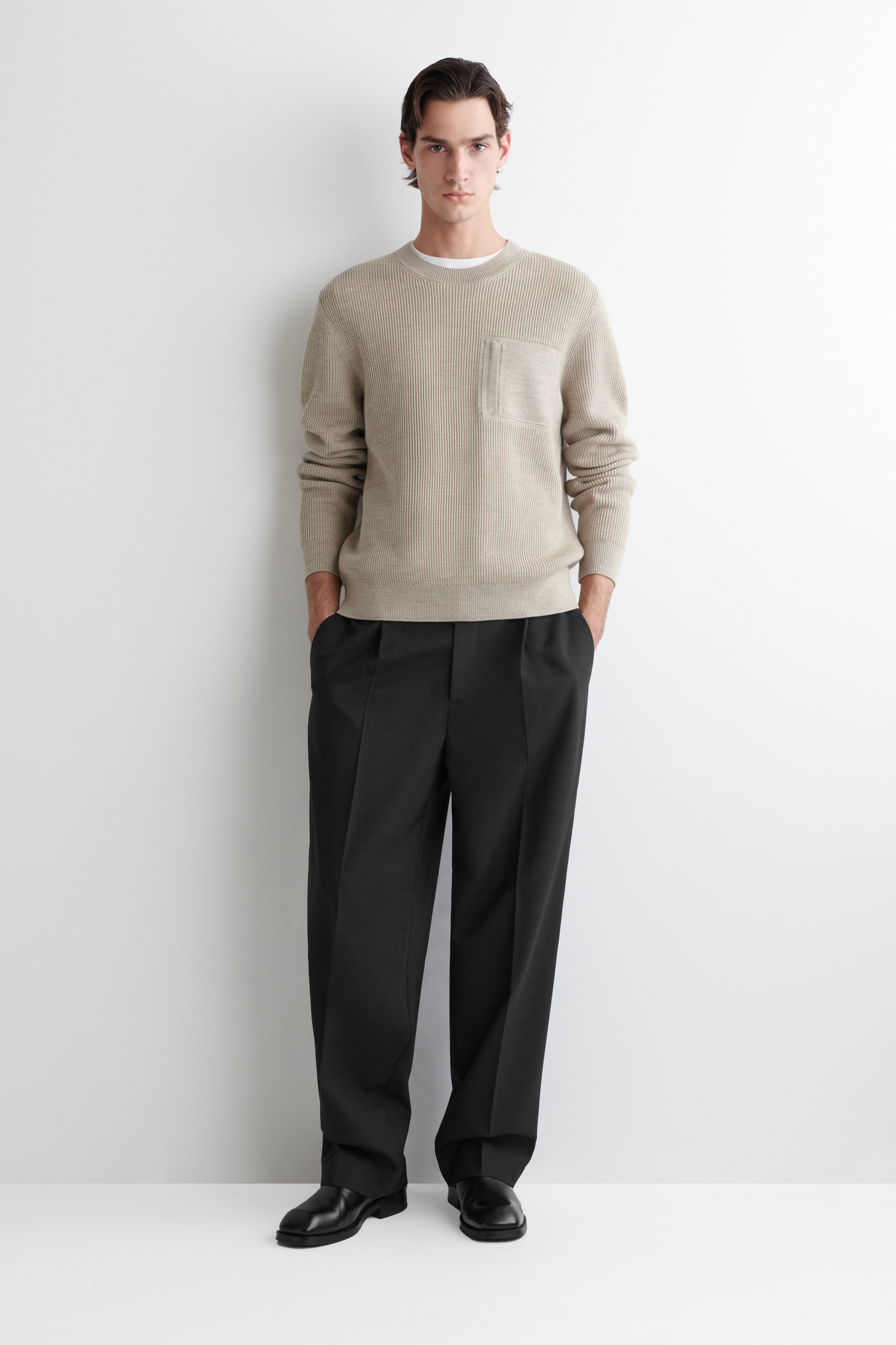 Agrandir l'image: Le PULL RAS DU COU EN LAINE AVEC DÉTAILS DE POCHE est présenté de FACE, mettant en valeur un tricot nervuré beige clair. Il présente un col rond avec un t-shirt blanc visible en dessous, une poche plaquée rectangulaire sur la poitrine gauche, des poignets nervurés et un ourlet nervuré.
