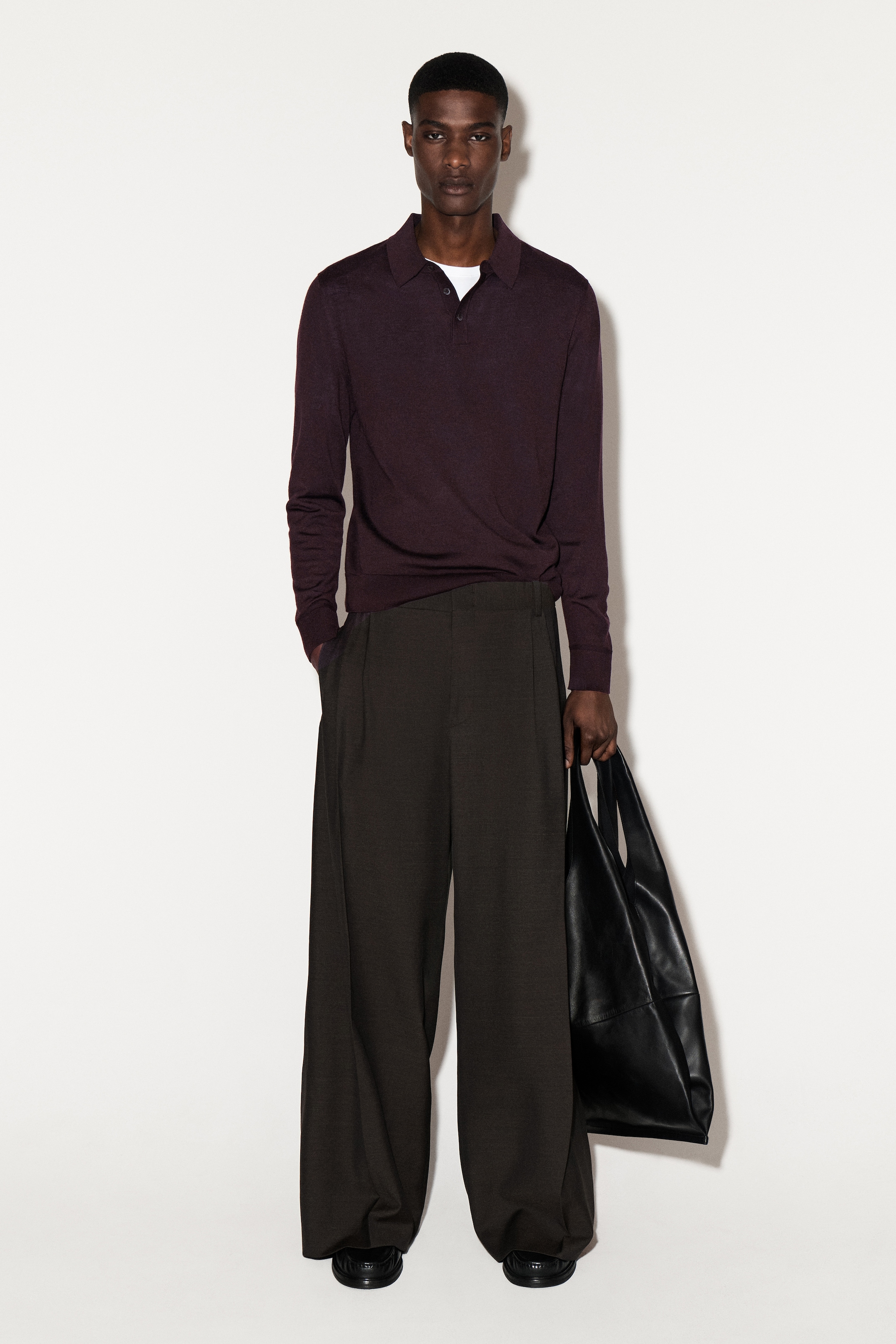 Visualizza immagine più grande: Una polo a maniche lunghe di colore bordeaux scuro viene indossata dalla parte anteriore, caratterizzata da un classico colletto polo e una chiusura a due bottoni sopra una t-shirt bianca. La camicia slim-fit ha polsini a coste e un orlo a coste.