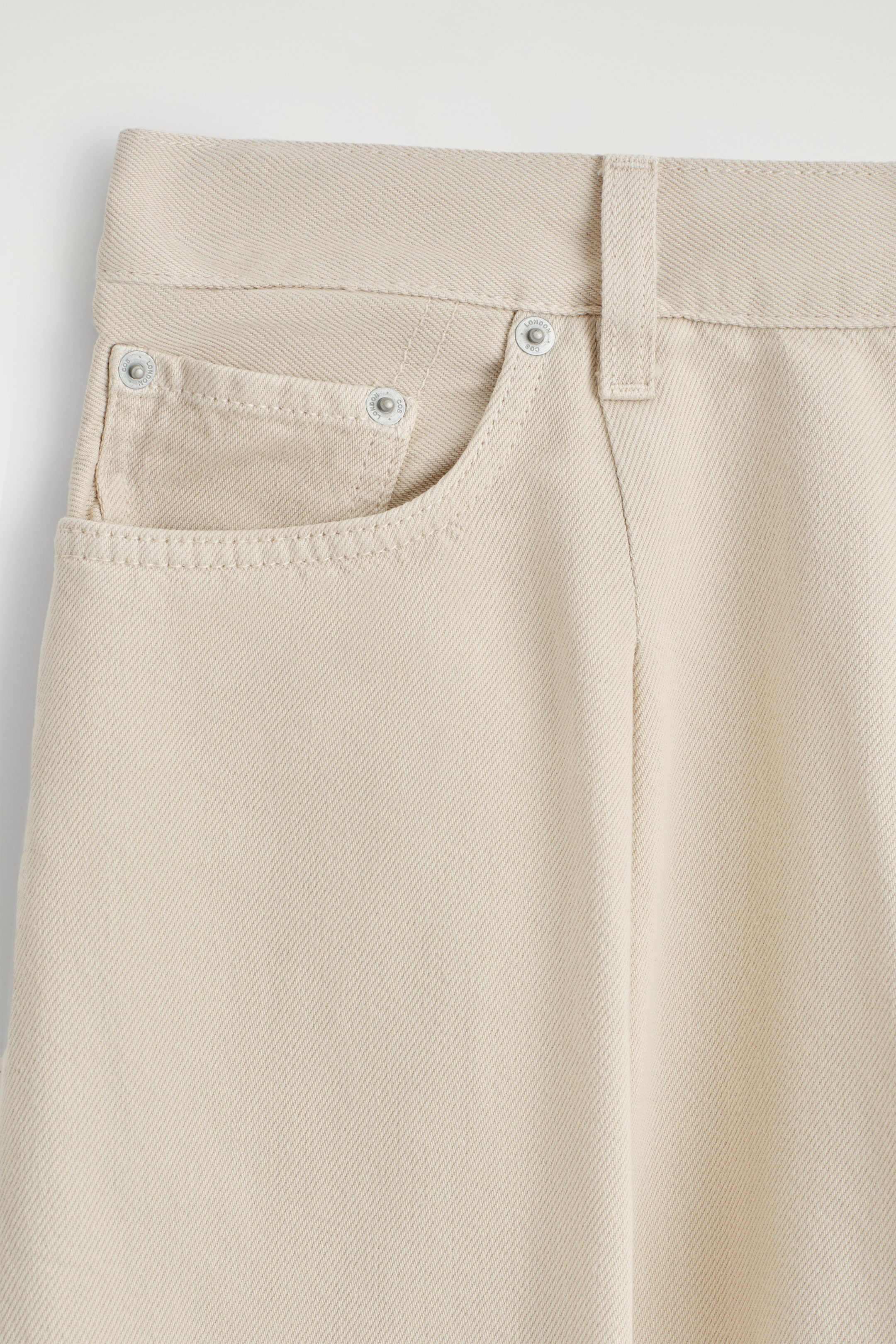 View larger image: The FRONT of the Twine jeans is displaying a dusty-pink hue, featuring a classic curved front pocket with a small coin pocket, both reinforced with metal rivets. A belt loop is visible on the waistband, and a subtle vertical pleat is running down the front leg.