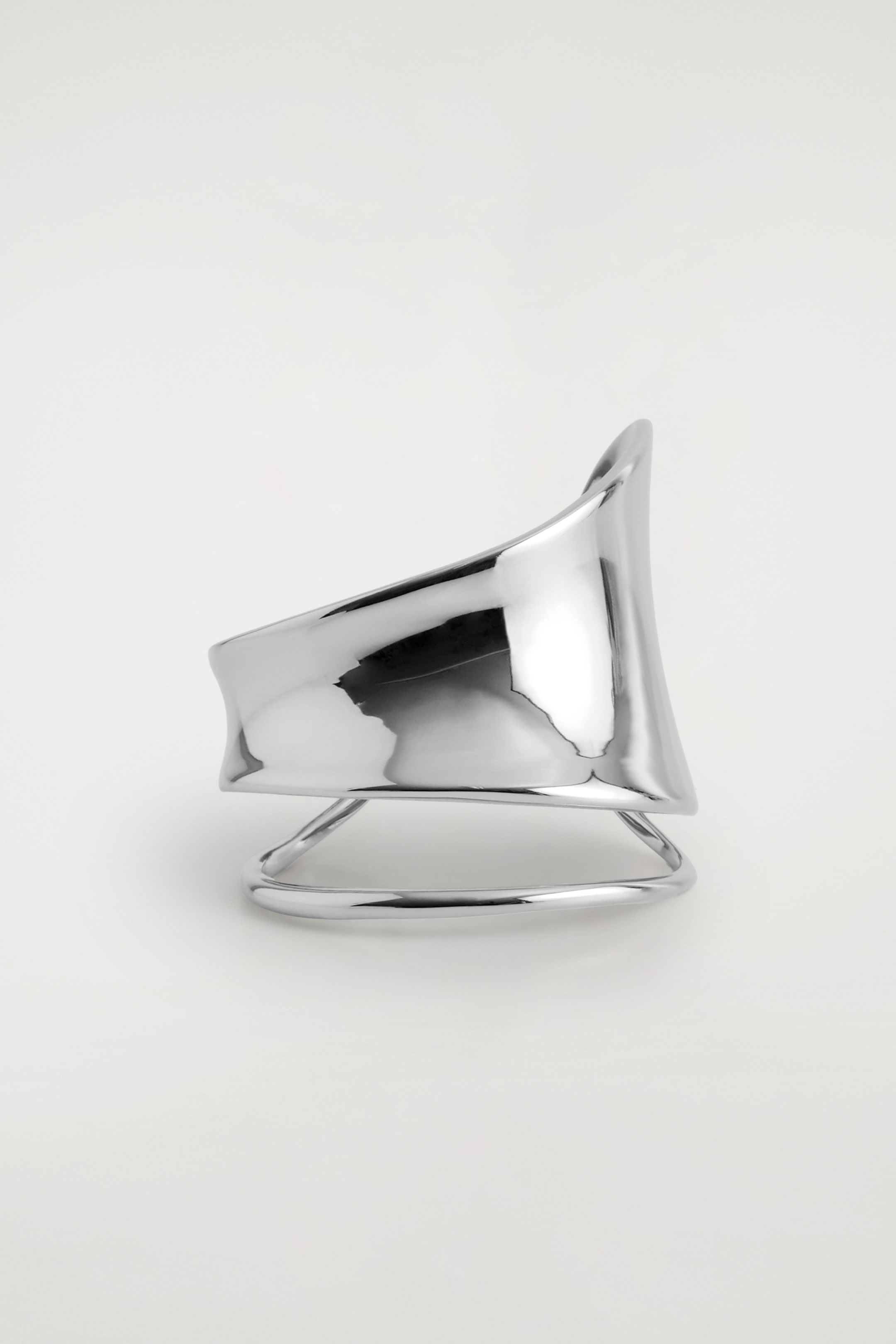 View larger image: A polished silver-toned cuff is displayed from the front, featuring a wide, sculptural upper band that is curving outwards above its distinctive double-wrap base.