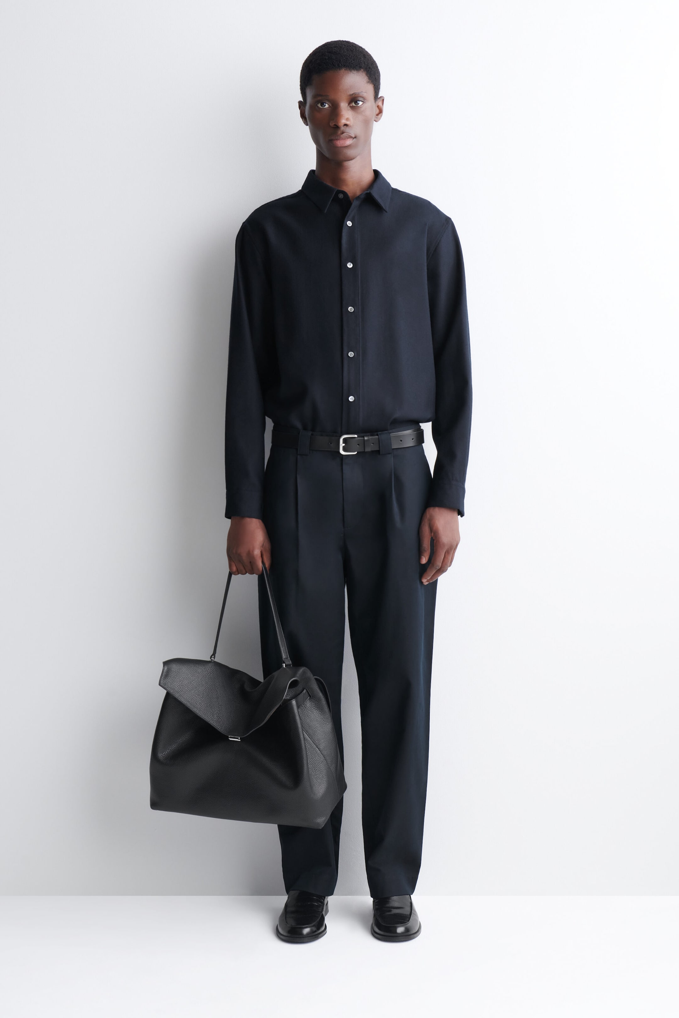 El bolso Trullo oversize con solapa en piel texturizada negra es sostenido por la modelo por sus finas asas superiores. El bolso presenta una solapa asimétrica plegada y una silueta relajada y desestructurada. El bolso Trullo oversize con solapa en piel texturizada negra es sostenido por la modelo por sus finas asas superiores. El bolso presenta una solapa asimétrica plegada y una silueta relajada y desestructurada.