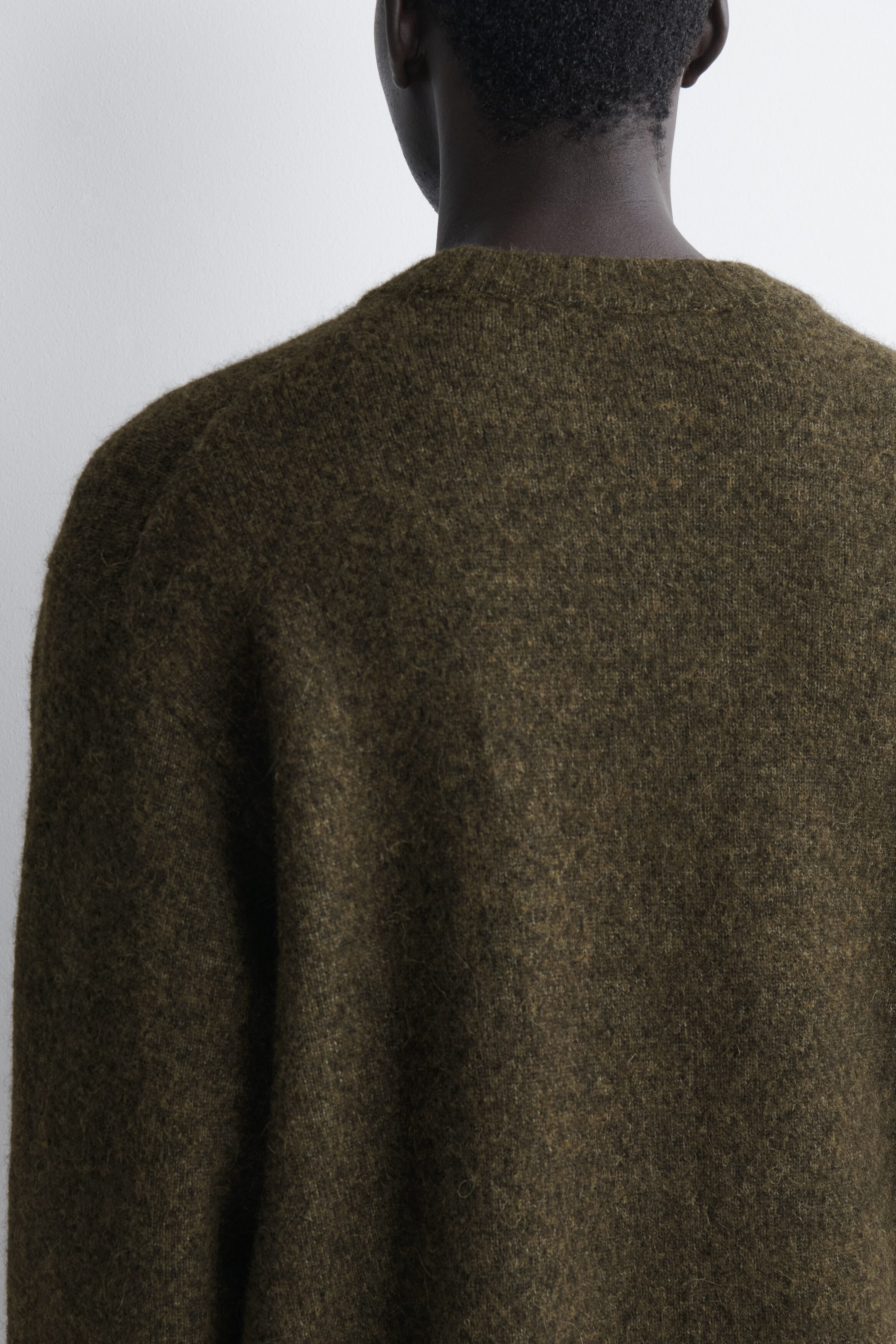 An oversized alpaca-blend crew-neck sweater is shown from the back, highlighting its fuzzy, textured olive-green knit and ribbed crew neckline. An oversized alpaca-blend crew-neck sweater is shown from the back, highlighting its fuzzy, textured olive-green knit and ribbed crew neckline.