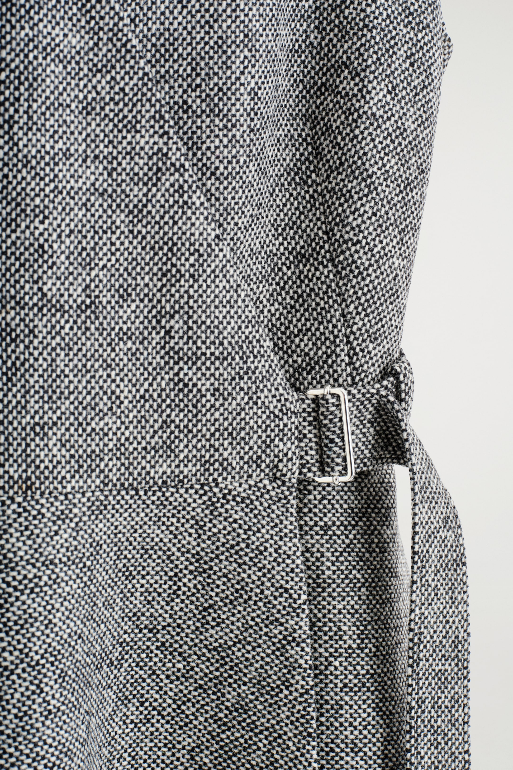 Ingrandisci l'immagine: L'abito mini in tweed misto lana presenta una texture nera e bianca a macchie. Una cintura in tessuto coordinato stringe la vita, fissata da una fibbia rettangolare in argento visibile sul lato.