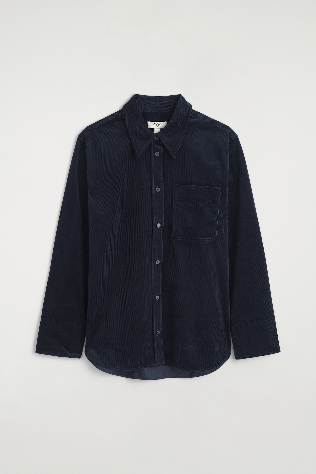 This dark navy cotton corduroy shirt is shown from the front, featuring a classic point collar, a button-front placket, and a single chest patch pocket. It features long sleeves with wide cuffs and a subtly curved hem.