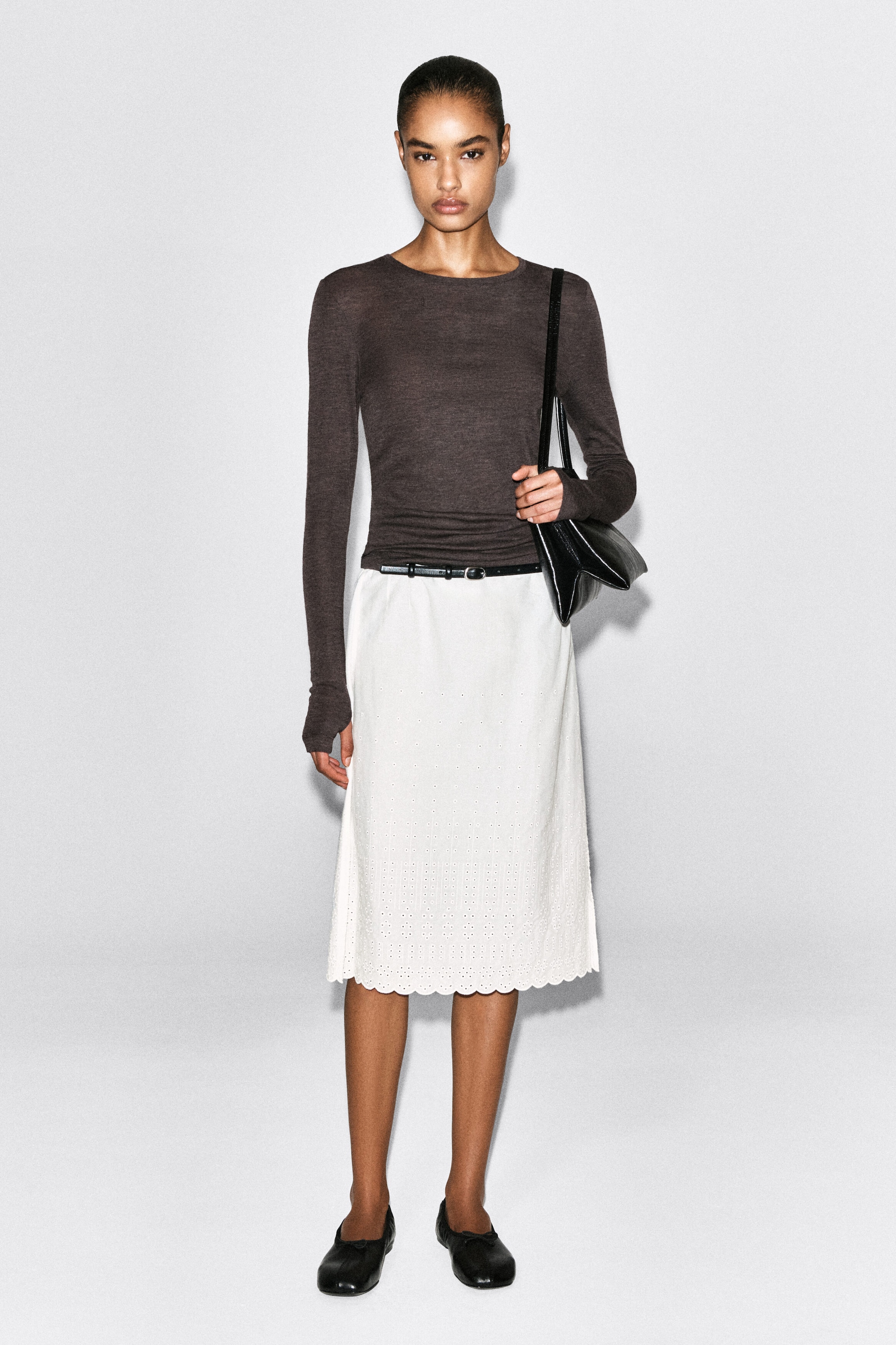 The slim merino wool top in dark brown is shown from the front, highlighting its lightweight, fine-knit texture and form-fitting silhouette. The top features a round neckline and extra-long sleeves, styled tucked into a white skirt. The slim merino wool top in dark brown is shown from the front, highlighting its lightweight, fine-knit texture and form-fitting silhouette. The top features a round neckline and extra-long sleeves, styled tucked into a white skirt.