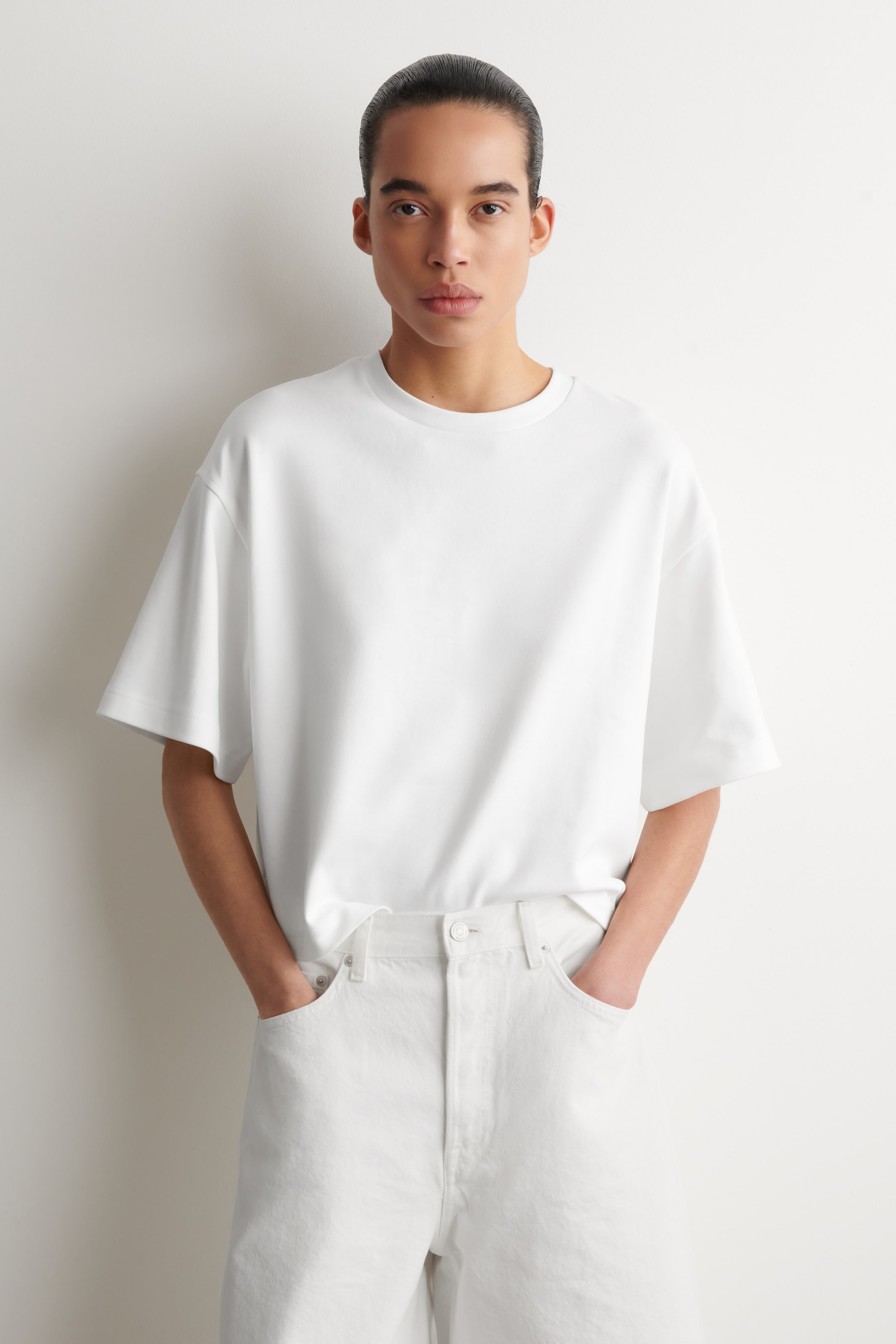 Visa större bild: En vit t-shirt med en oversized passform, rund hals och korta, vida ärmar, visar sin fram- och sidoprofil. Den har en rak fåll och bärs utan att vara instoppad.