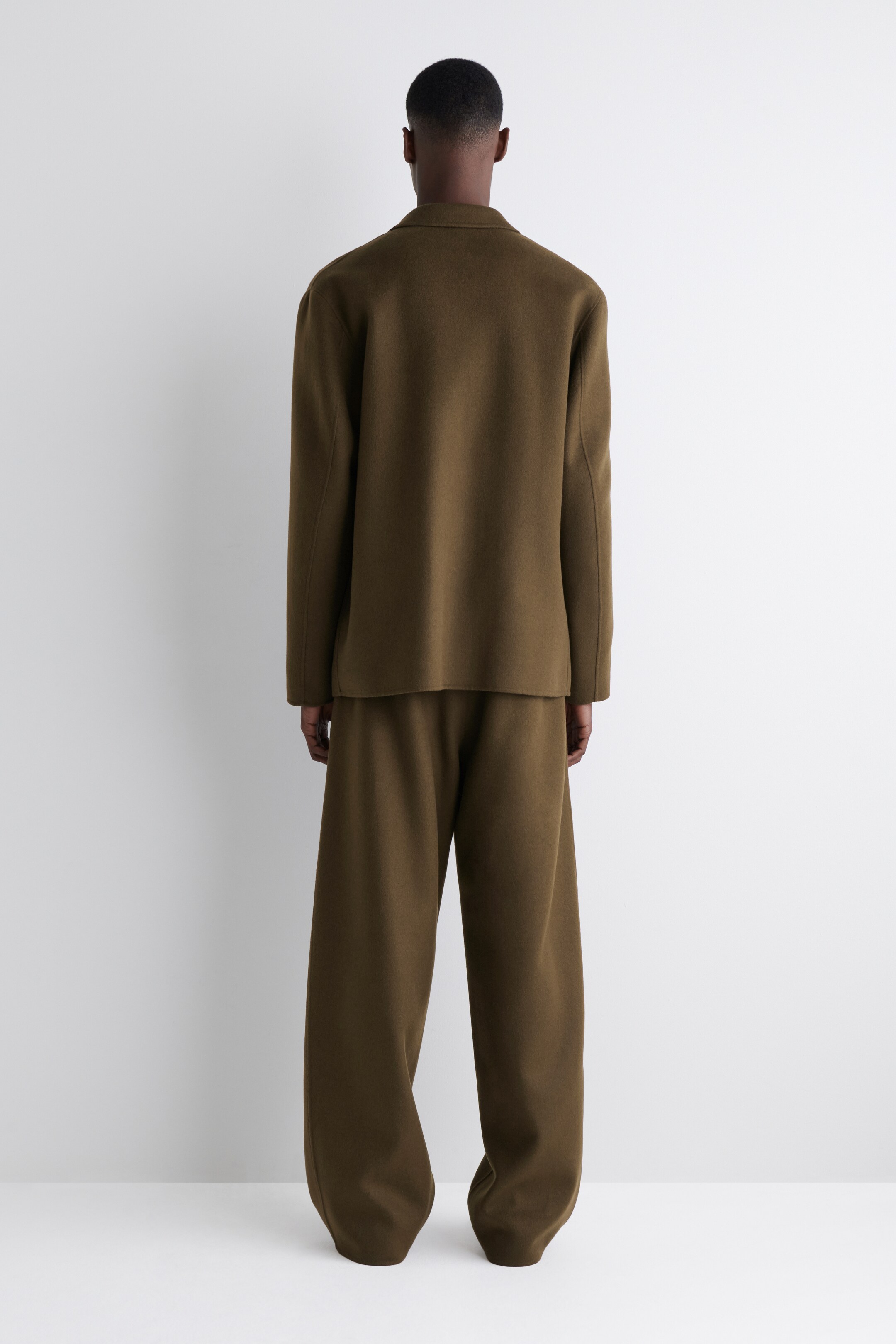 Agrandir l'image: Un ensemble deux pièces vert olive foncé est présenté de dos, mettant en valeur un tissu doux et fluide. La veste à coupe décontractée présente un col structuré et des épaules tombantes, et le pantalon large assorti s'accumule aux chevilles.