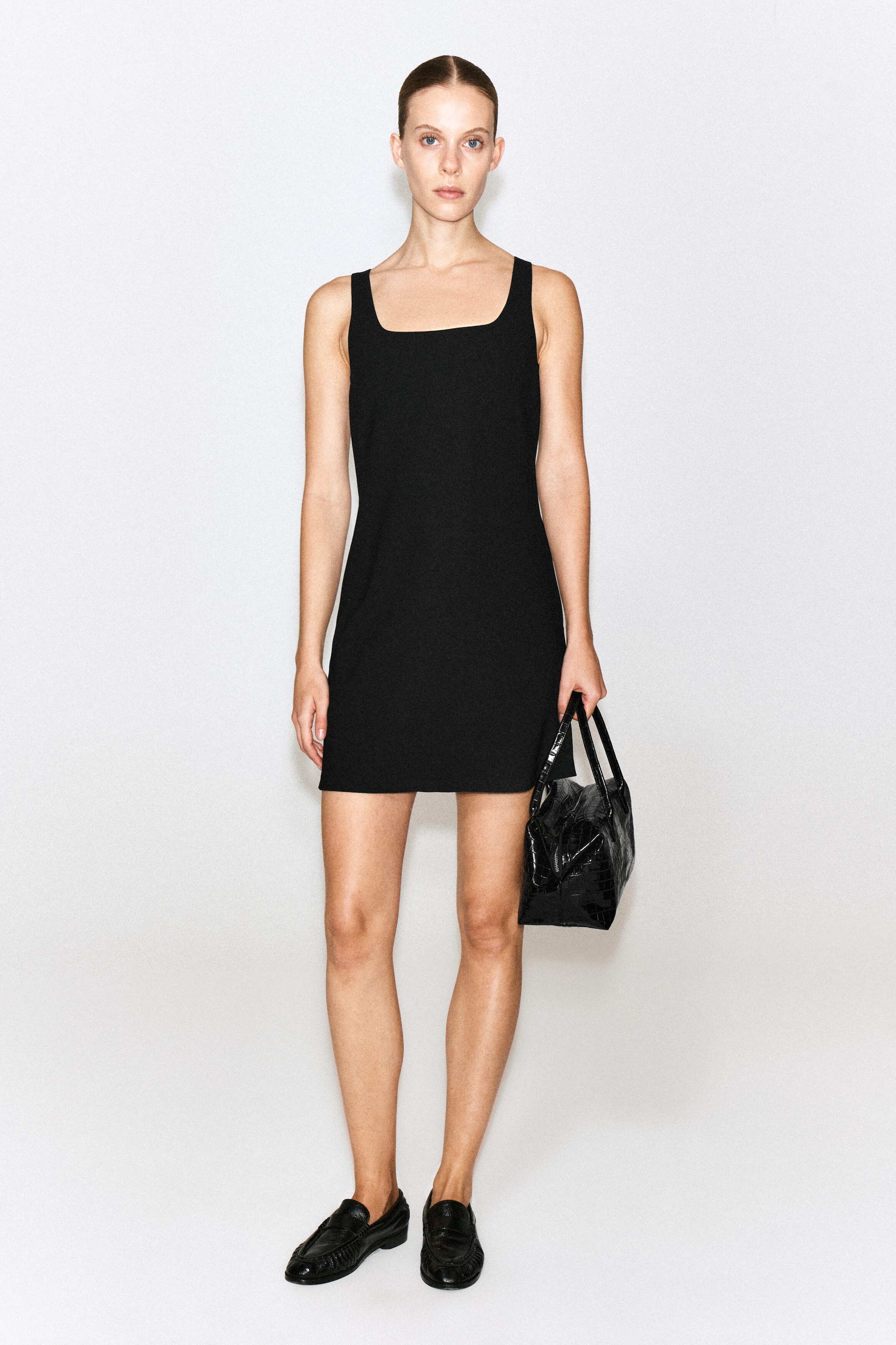 The square-neck crepe jersey dress, front-facing, showcases a sleeveless design with wide shoulder straps and a square neckline. The dress falls to a mini length with a straight-cut silhouette. The square-neck crepe jersey dress, front-facing, showcases a sleeveless design with wide shoulder straps and a square neckline. The dress falls to a mini length with a straight-cut silhouette.