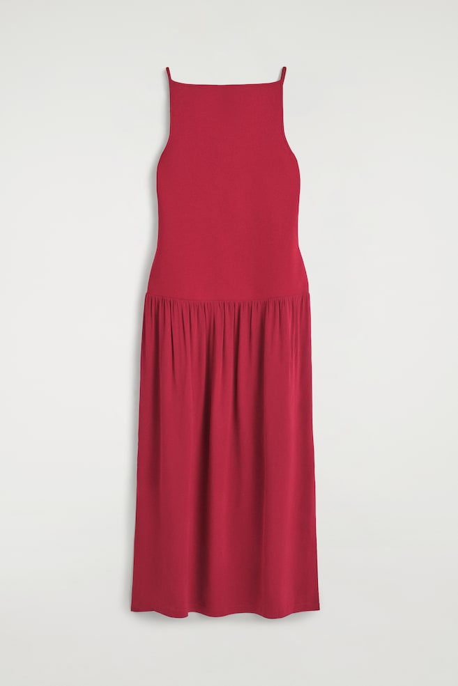 O vestido maxi com painéis em contraste, numa tonalidade de vermelho profundo, está pendurado em vista frontal, apresentando um corpete ajustado com decote direito e alças finas. O corpete faz a transição, numa linha de cintura descaÃda, para uma saia maxi franzida e fluida. - 1