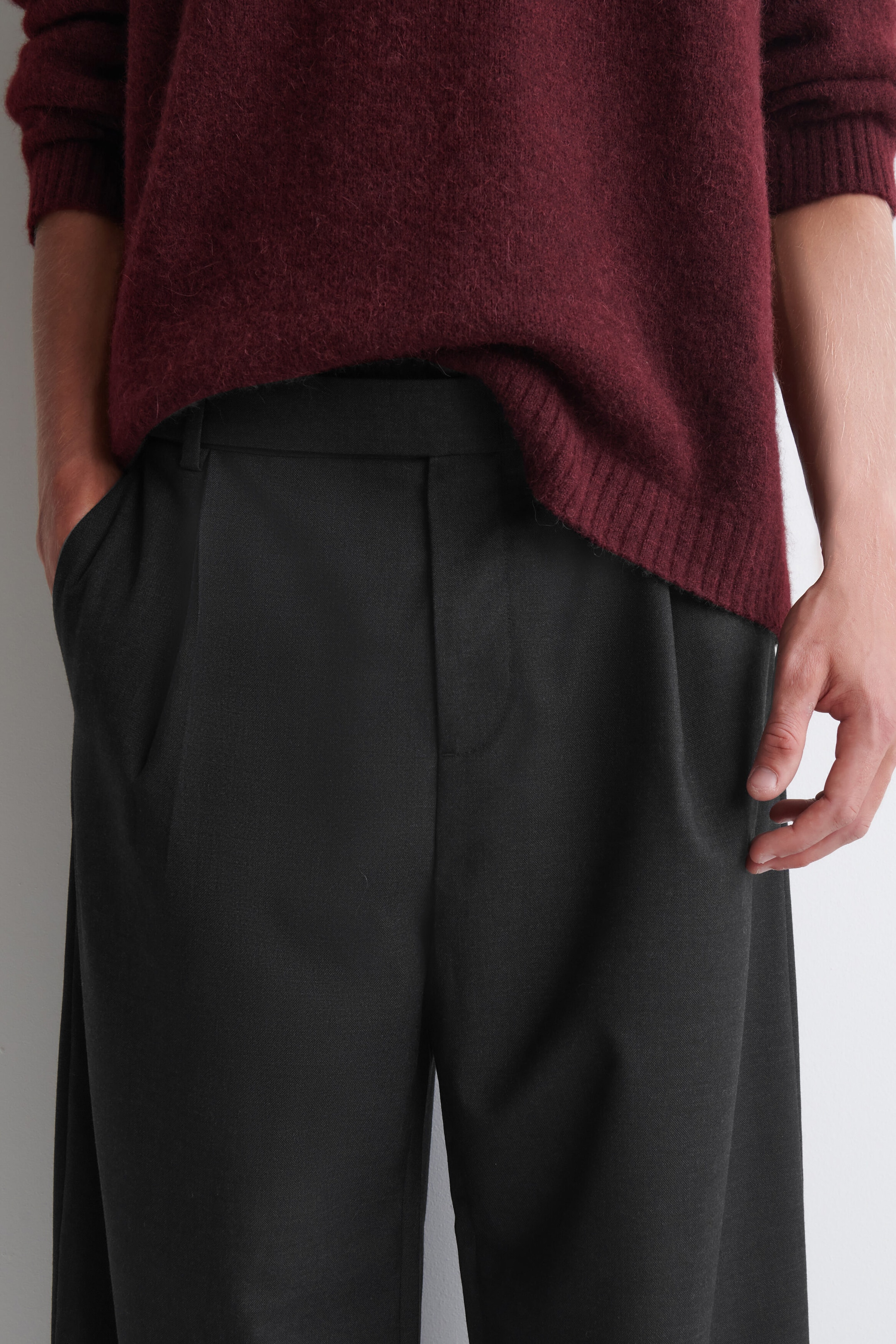 The belt-detail wool relaxed-fit barrel-leg trousers in dark grey feature structured front pleats, side pockets, and a clean waistband. A burgundy knit jumper is partially tucked into the waistband, highlighting the trousers' relaxed fit and soft wool construction. The belt-detail wool relaxed-fit barrel-leg trousers in dark grey feature structured front pleats, side pockets, and a clean waistband. A burgundy knit jumper is partially tucked into the waistband, highlighting the trousers' relaxed fit and soft wool construction.
