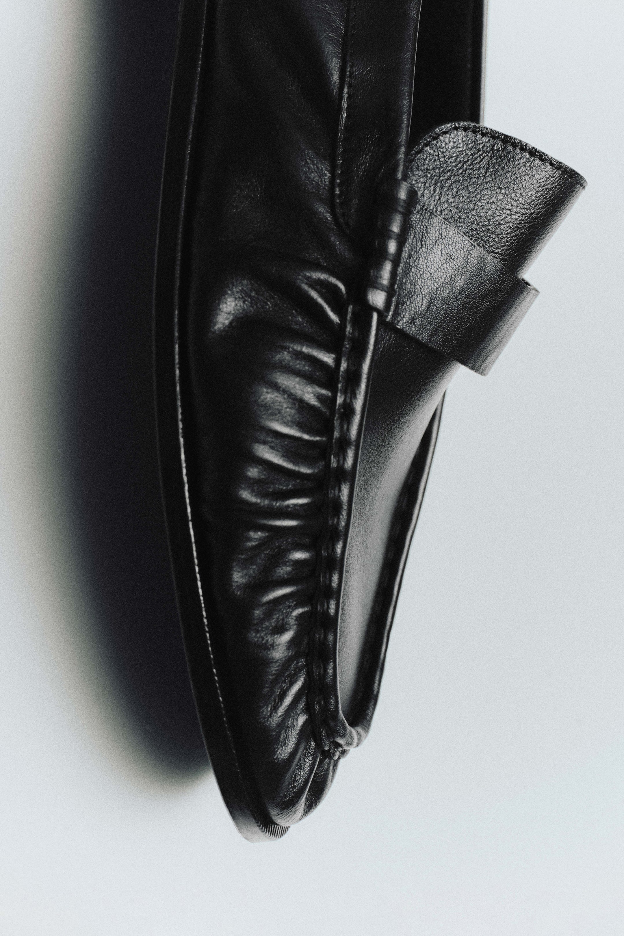 Größeres Bild ansehen: Ein schwarzer Lederslipper ist in einer Nahaufnahme zu sehen, die die weich gerafften Lederdetails im Zehenbereich sowie den klassischen Penny-Riemen über dem Vorderblatt hervorhebt.