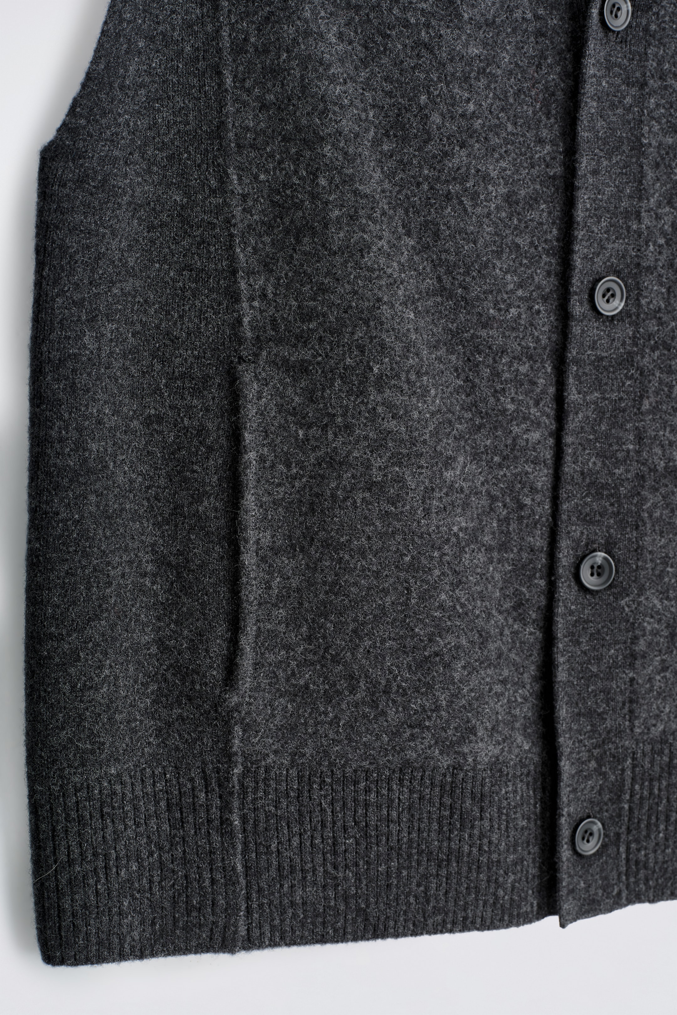 View larger image: A dark gray buttoned vest is being shown from the FRONT, featuring a soft, felted texture. It is displaying a vertical button placket with dark circular buttons, subtle vertical seam details, discreet pocket openings, and a ribbed bottom hem.